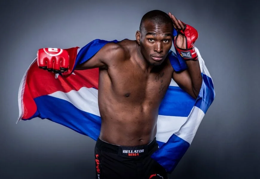 Mixed martial artist posing with a Costa Rican flag draped over his shoulders, wearing red gloves and shorts, in a fighting stance, against a gray background.