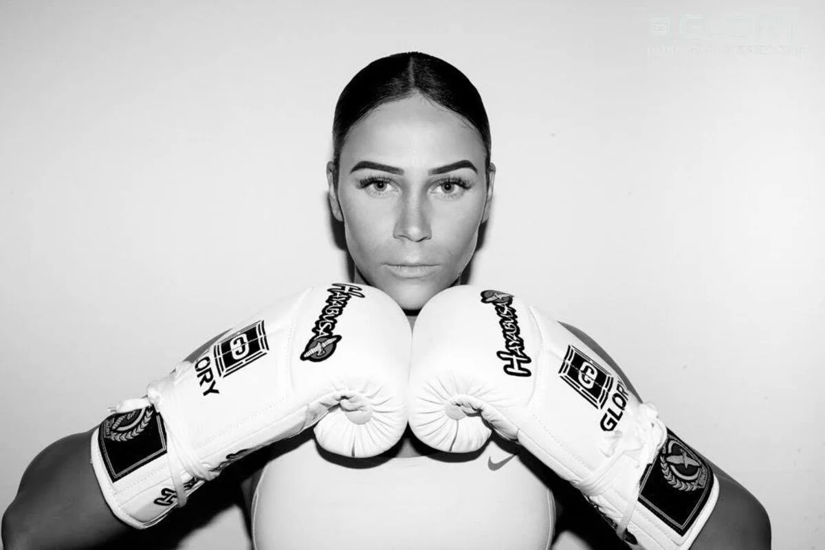 Black and white photo of a female boxer wearing boxing gloves, facing forward with a serious expression.