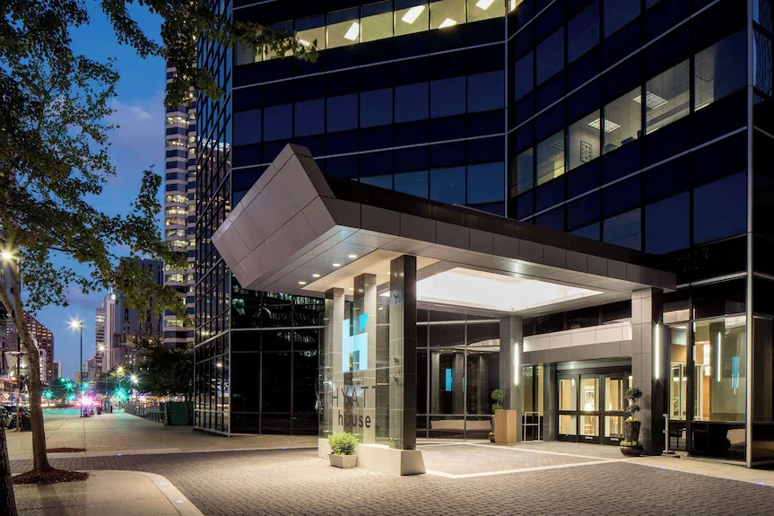 Exterior of a Hyatt hotel building at dusk with glass windows, trees, and city lights.