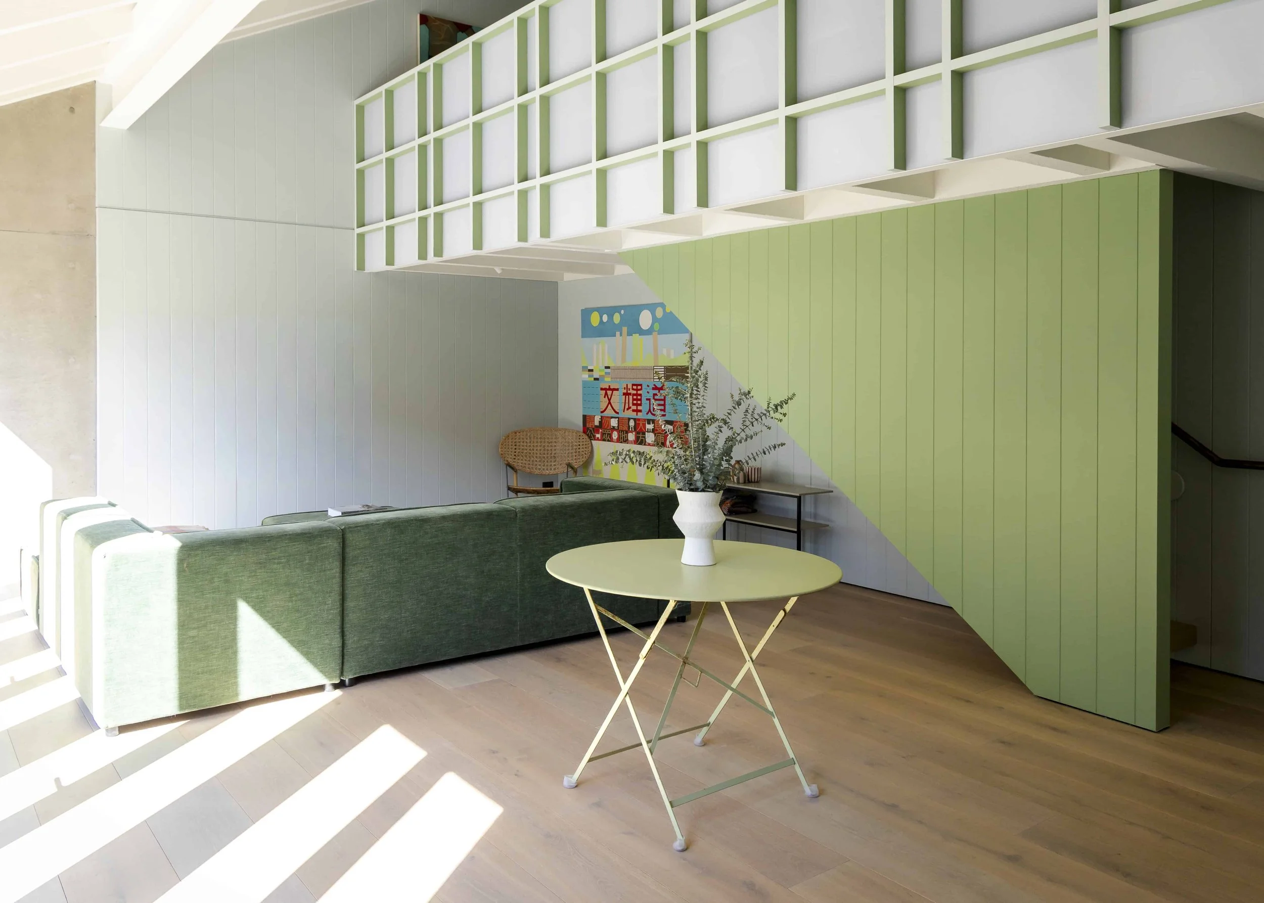 Modern interior with a green sofa, a yellow folding table with a white vase and plant, a wall with green and white panels, and a colorful artwork.
