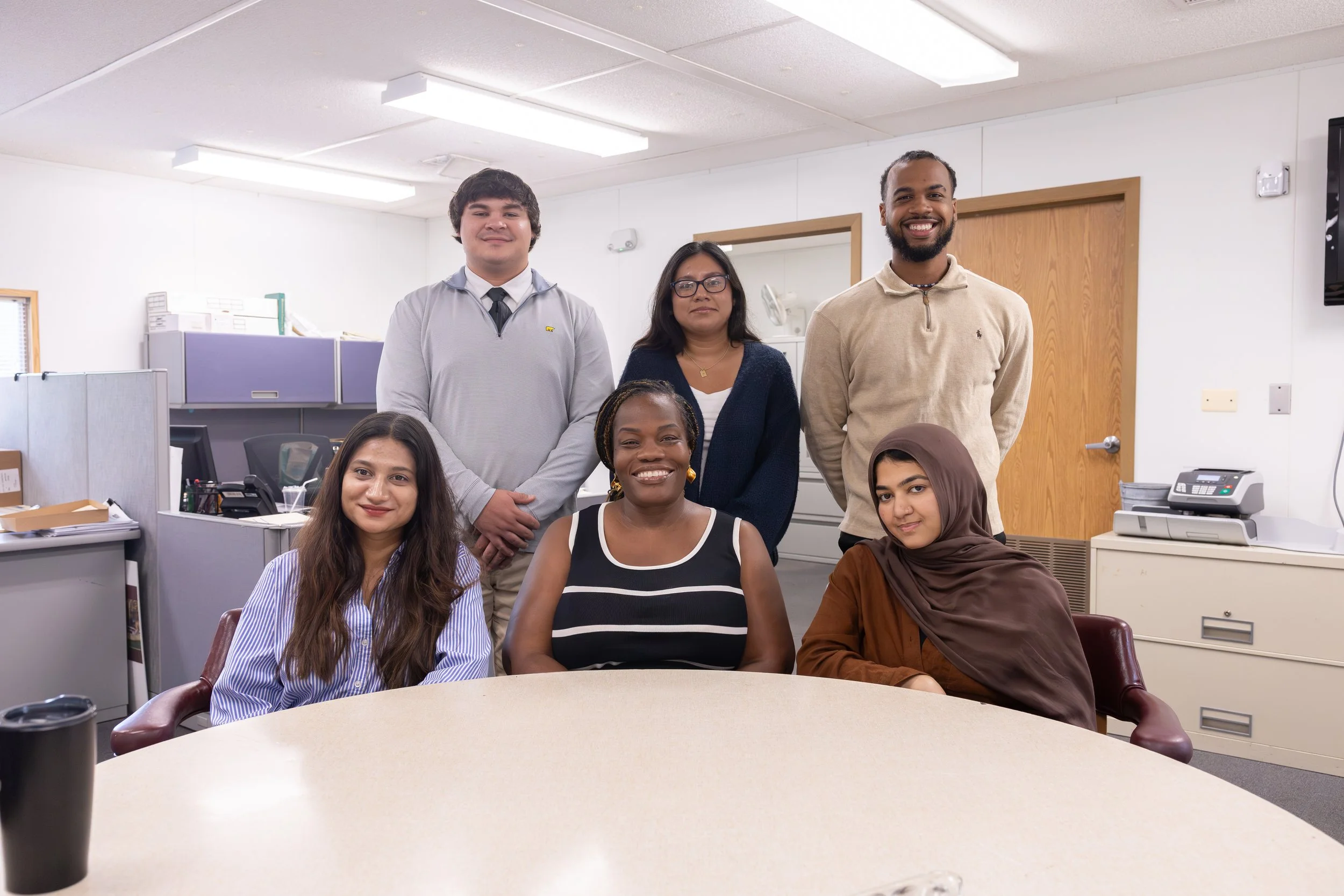 Group of seven diverse professionals posing for a photo in an office conference room, smiling and looking at the camera.