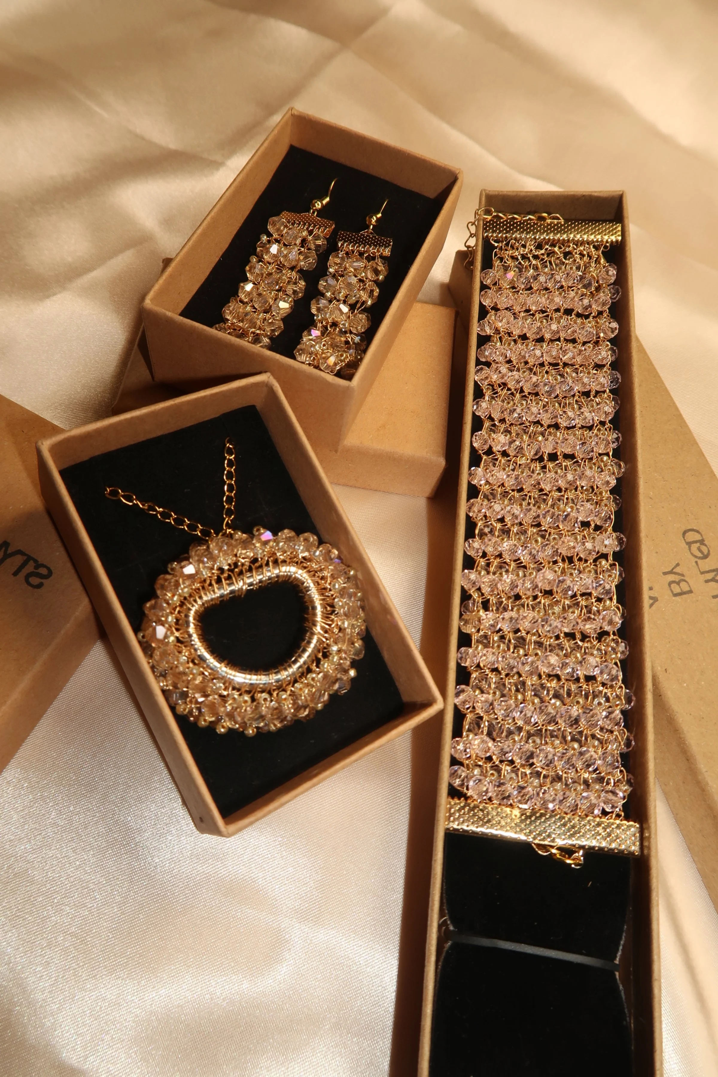 Gold jewelry set including earrings, bracelet, and necklace with clear gemstones, displayed in jewelry boxes.