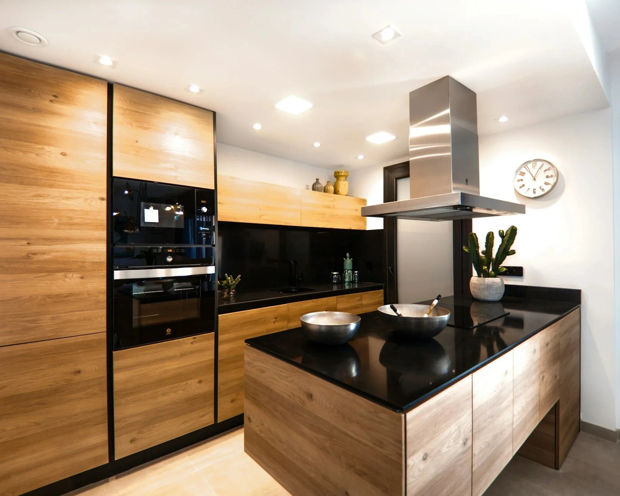 Modern kitchen with wooden cabinets, black countertop, a stainless steel range hood, and a cactus plant on the counter.