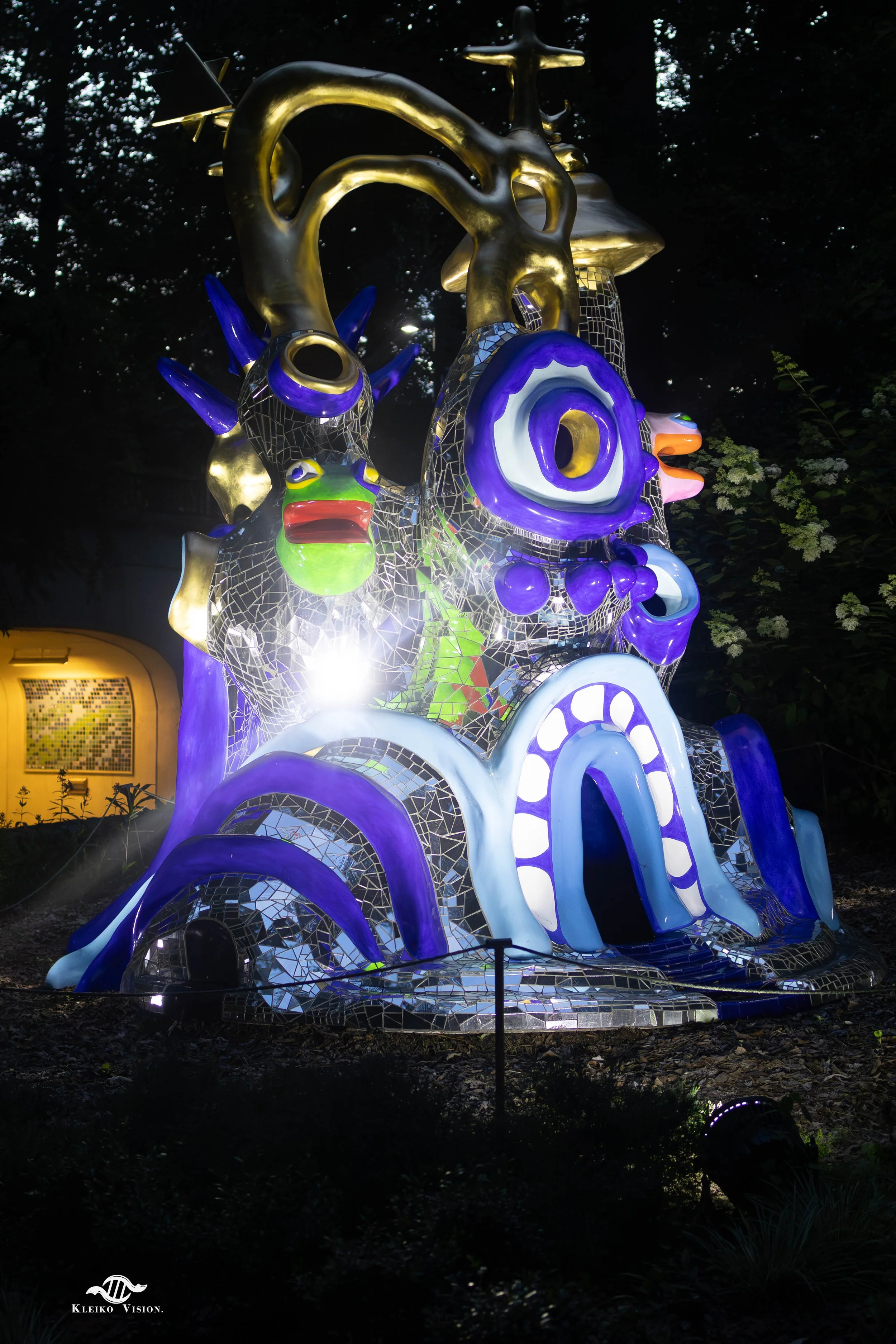Illuminated mirror-mosaic dragon sculpture glowing purple and gold at night