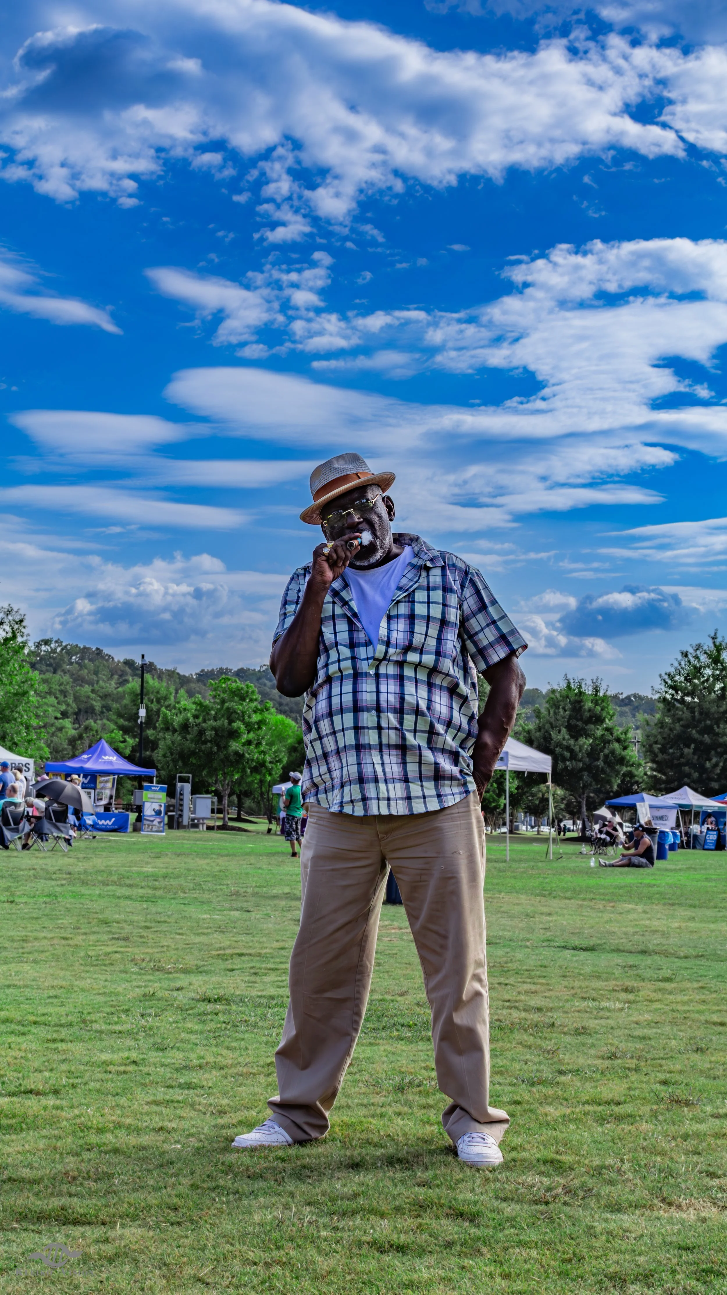 Man in a straw hat smoking a cigar at an outdoor community festival