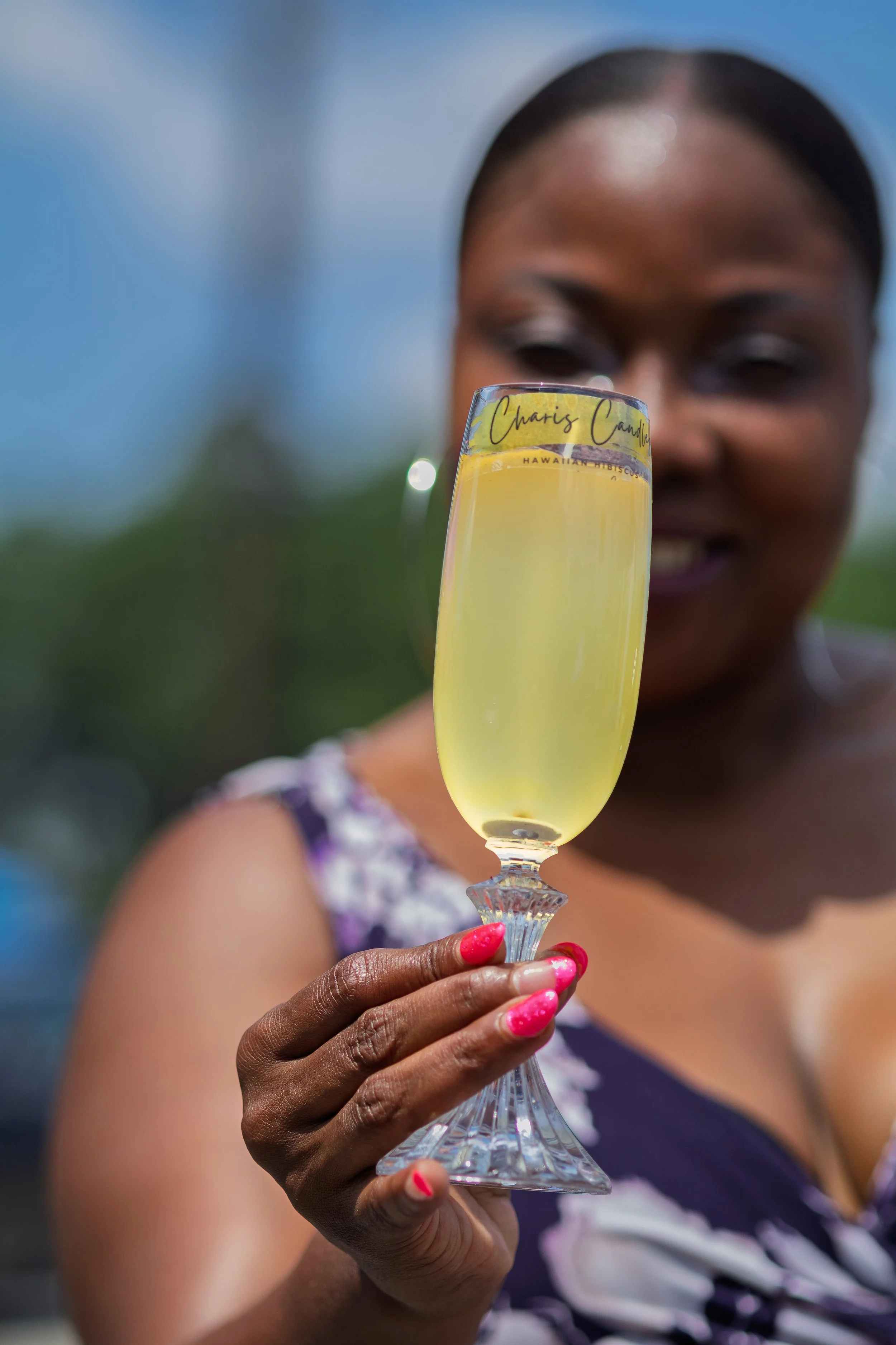 Woman holding a flute of sparkling hibiscus mocktail in outdoor sunlight