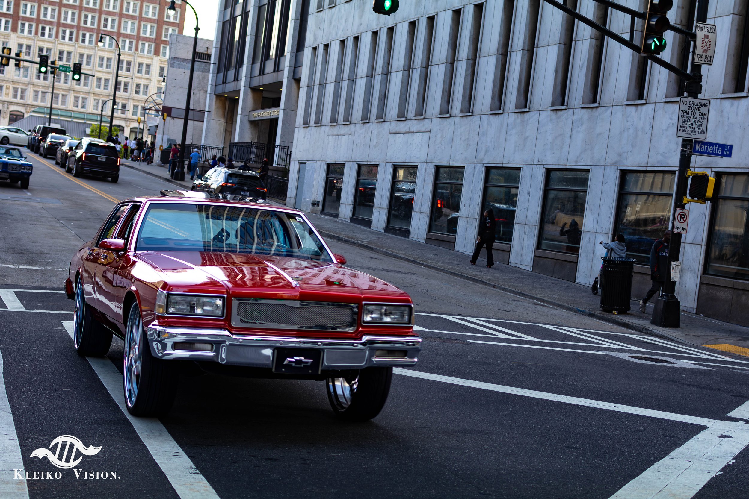 Custom red 1980s Chevrolet Caprice lowrider cruising through downtown Atlanta at dusk