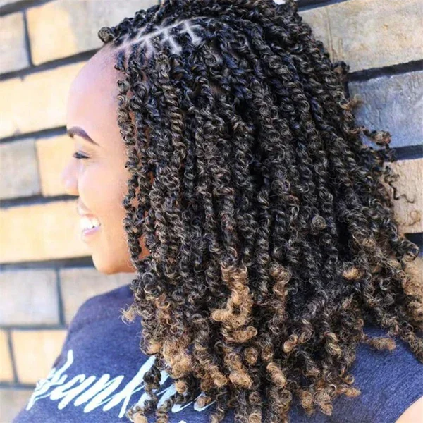 A woman with curly, dark brown hair with blonde tips, smiling and resting her head against a brick wall.