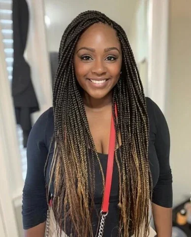 Smiling woman with long braided hair wearing a black top and red lanyard in a hallway.