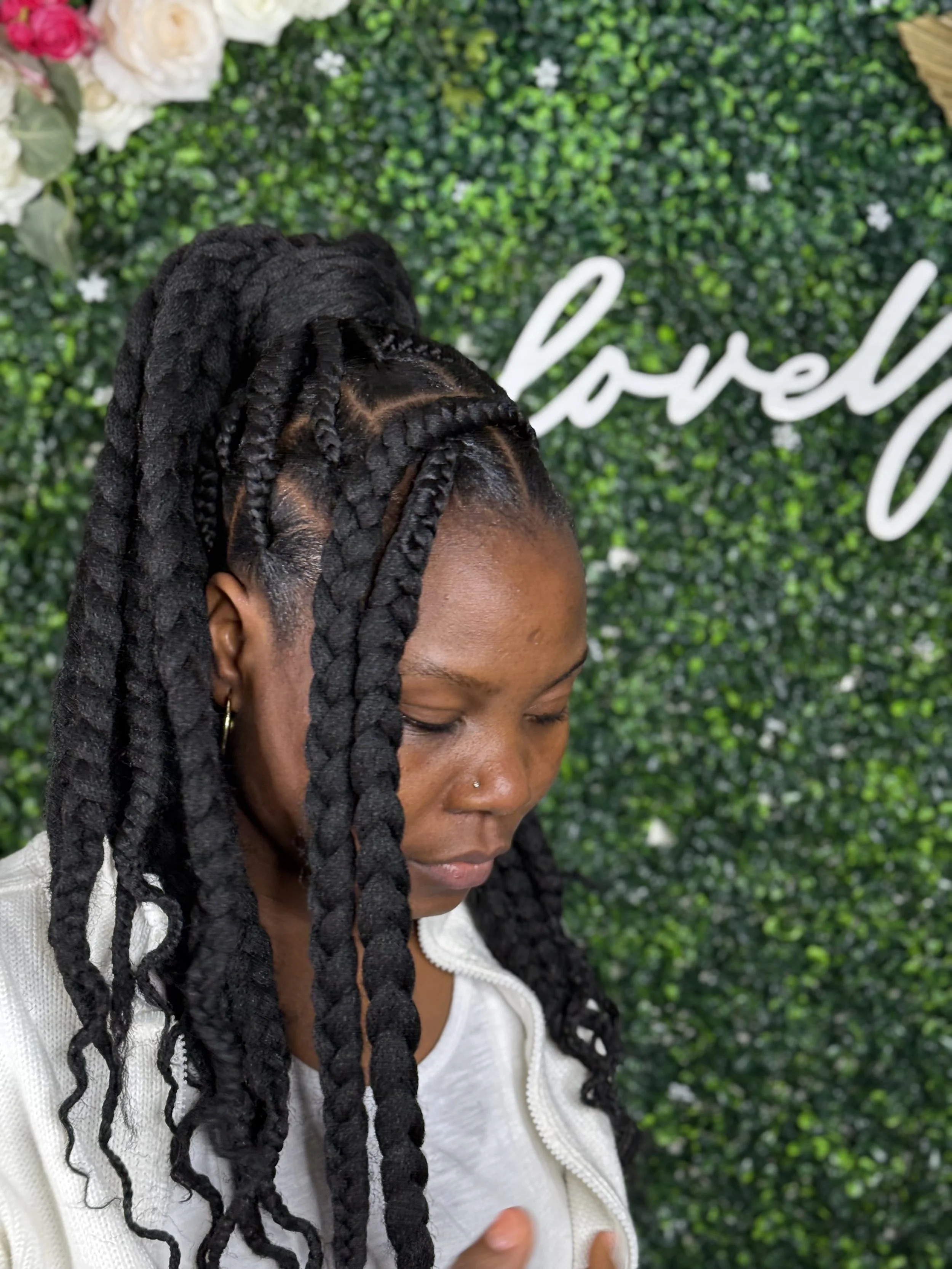 Woman with braided hairstyle in front of a green bush wall with the word 'love' written on it.