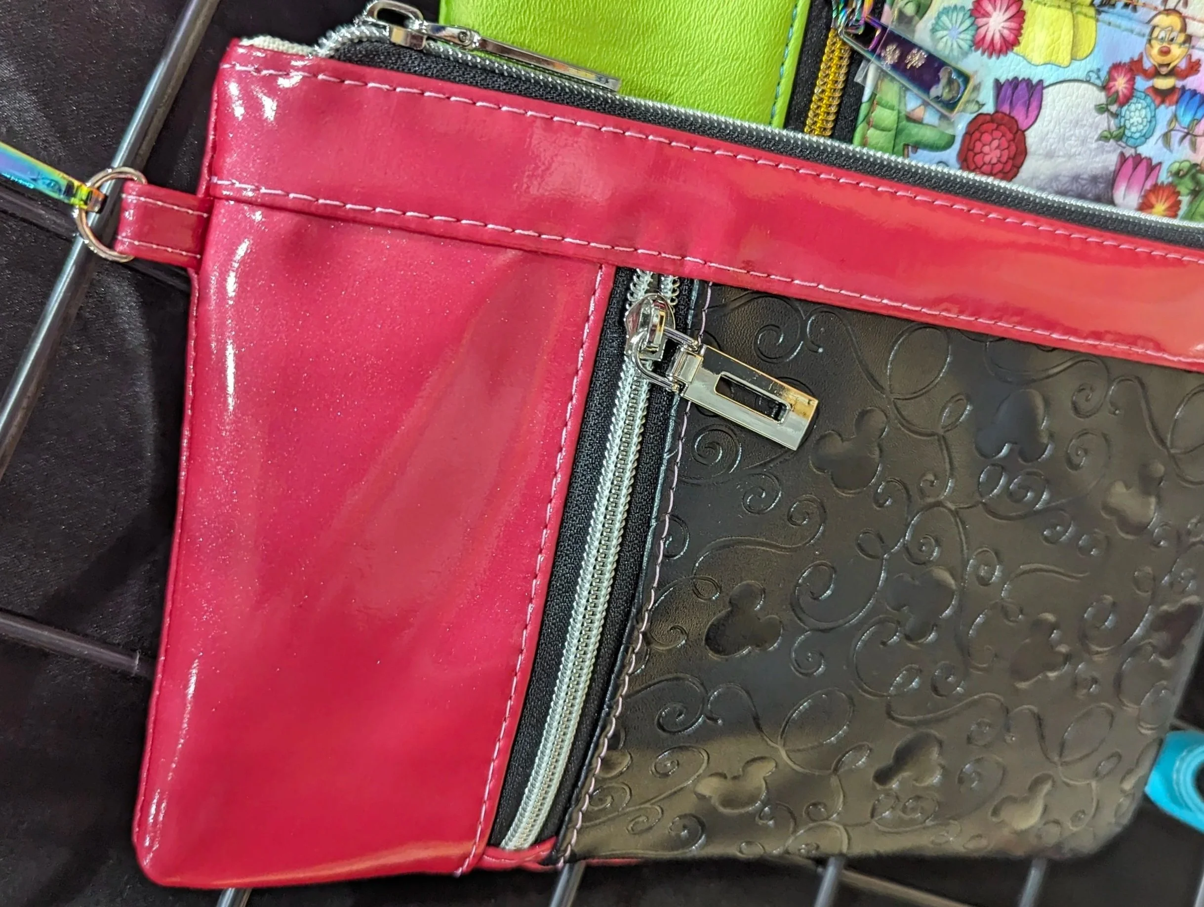 Close-up of a colorful handbag with red, black, and green sections, textural patterns, zippers, and a floral fabric lining.