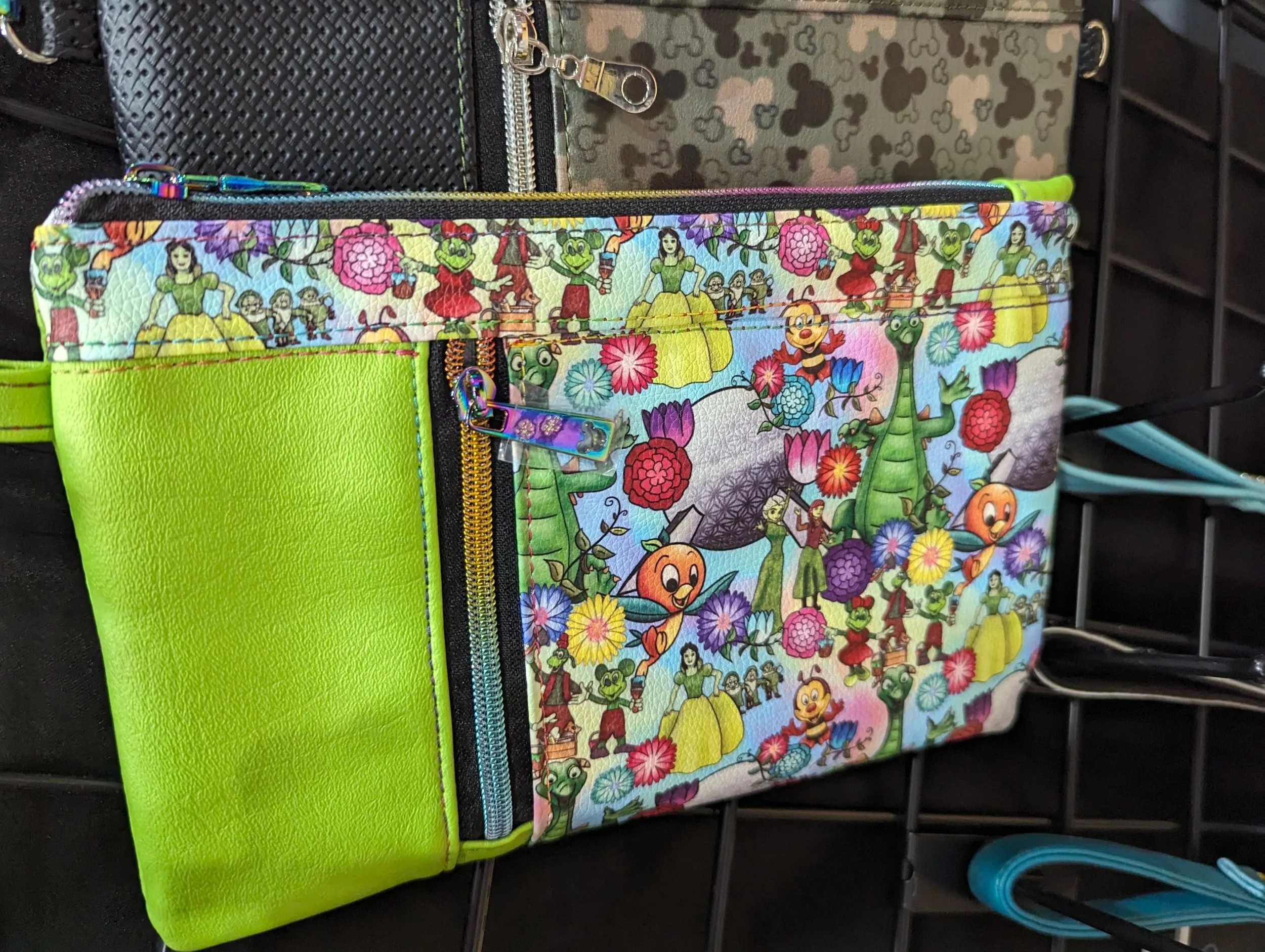 A colorful shoulder bag with a vibrant Sesame Street pattern featuring characters like Big Bird, Elmo, Oscar the Grouch, and others, with a bright green accent on the side and a zipper pocket.
