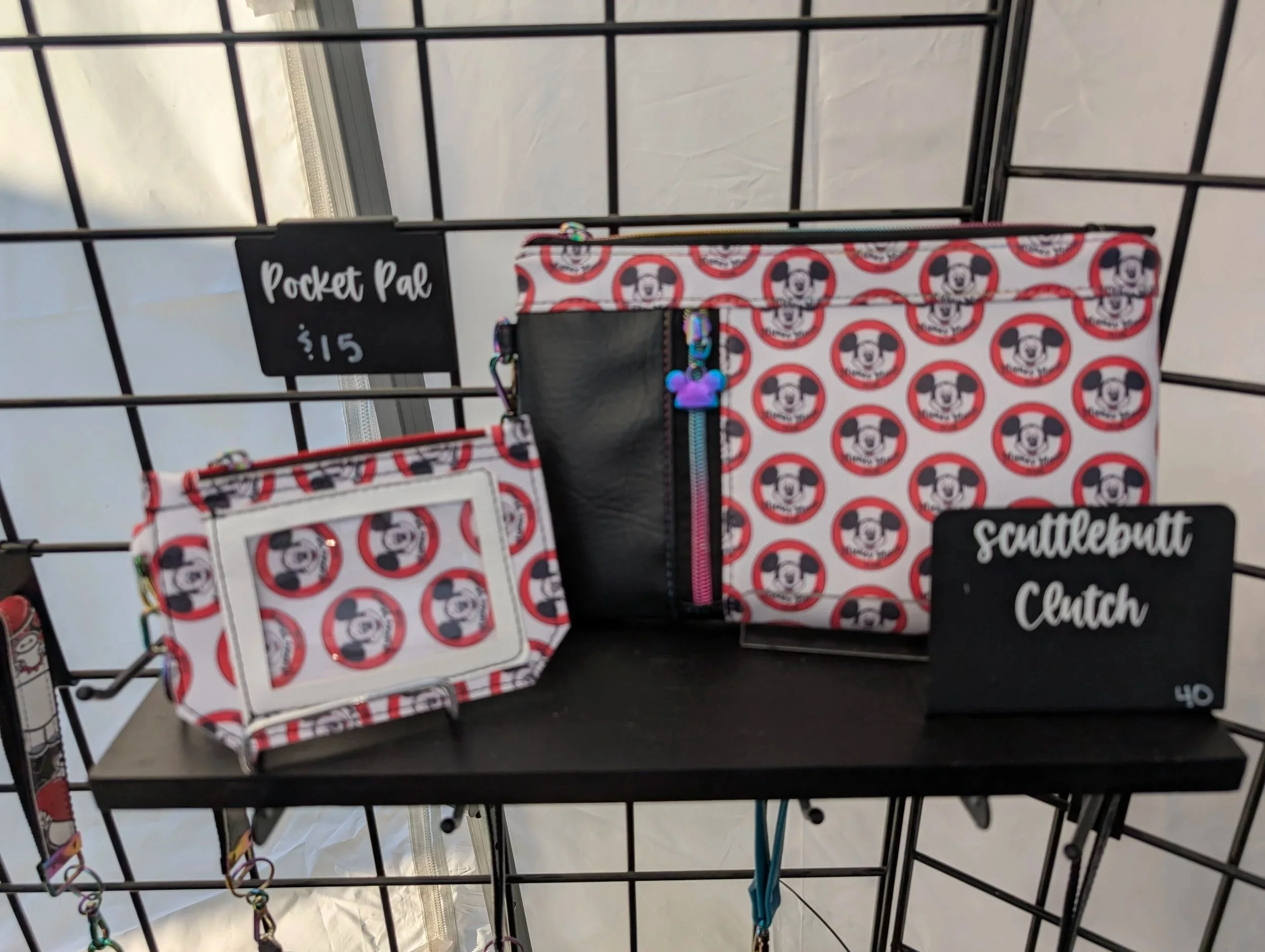 Display of Mickey Mouse themed pocket pal and scuttlebutt clutch bags on a black wire shelf, with a black sign indicating prices of $15 and $40.