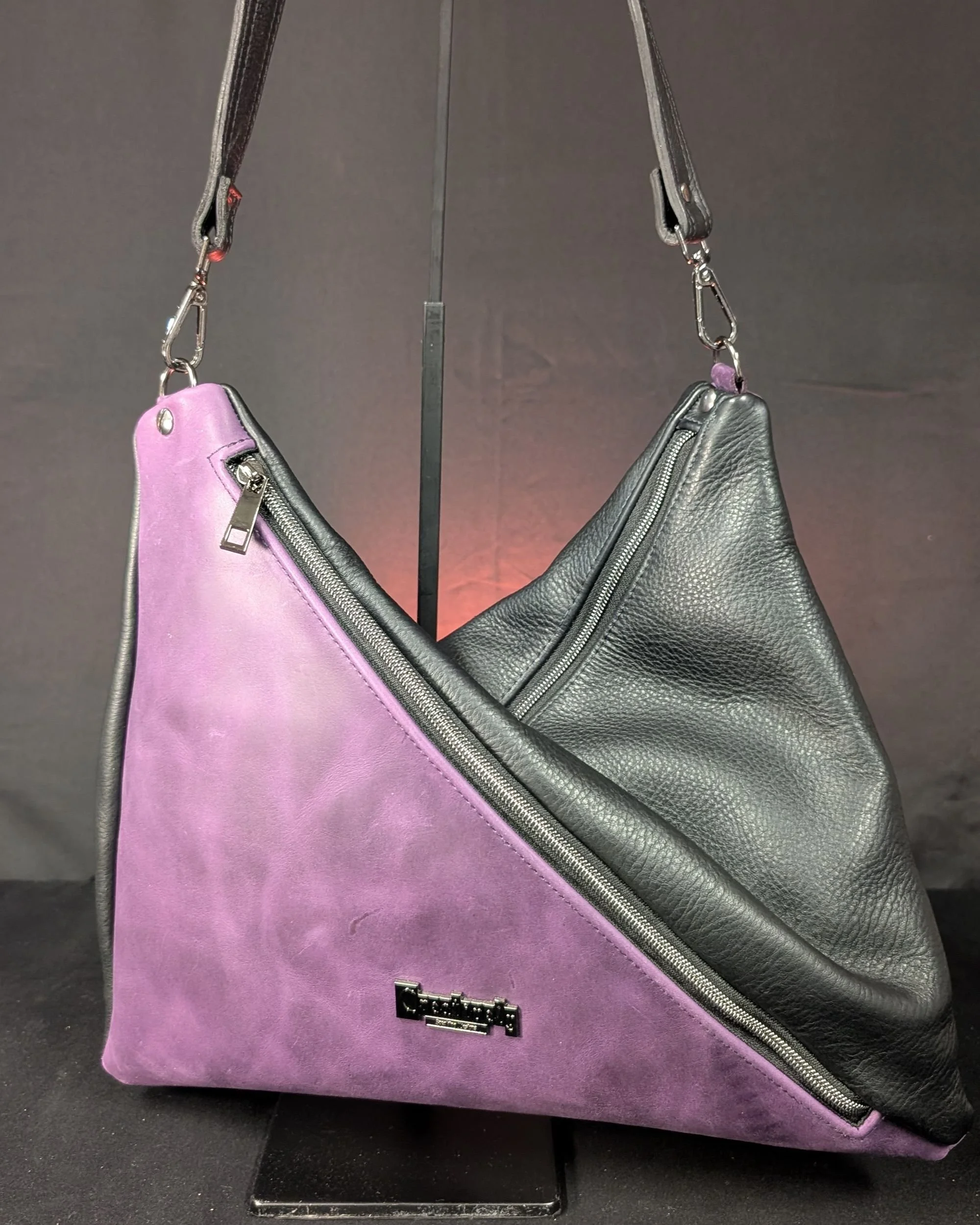 Handmade "Persuasion" triangle tote with leather featuring a two tone purple and black design, crafted by Creatively Speaking Designs.