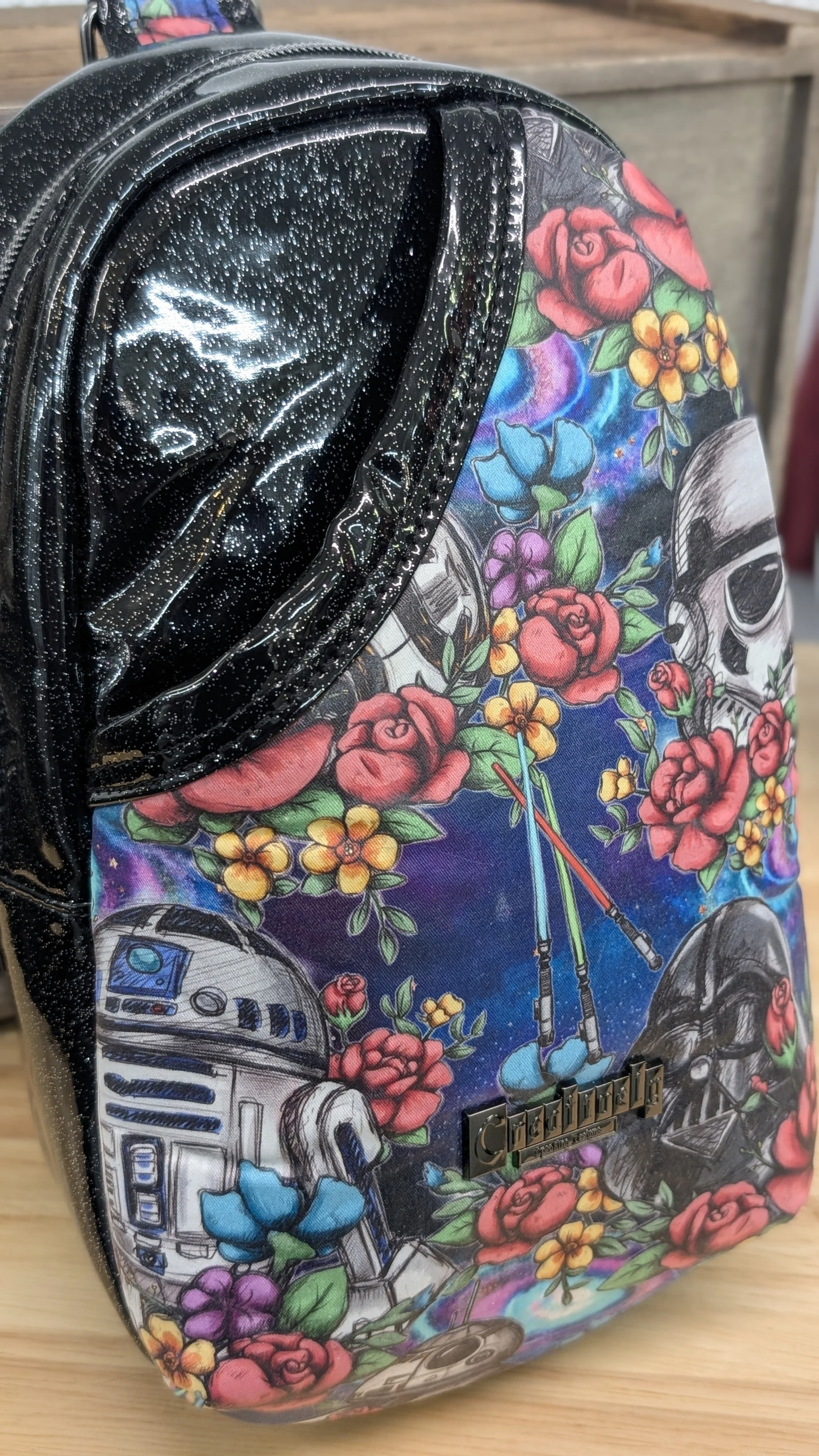 A colorful backpack featuring Star Wars characters like Darth Vader and R2-D2 surrounded by vibrant flowers and skull designs.
