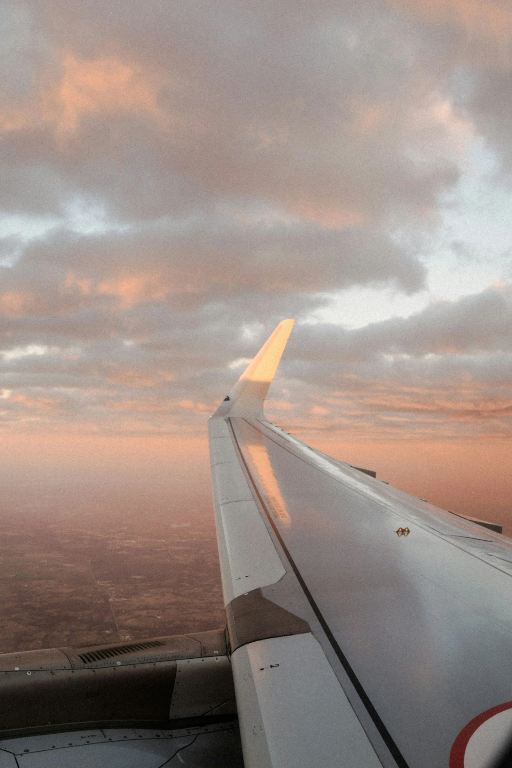 View from an airplane window showing the wing of the aircraft with a sunset sky and clouds in the background.