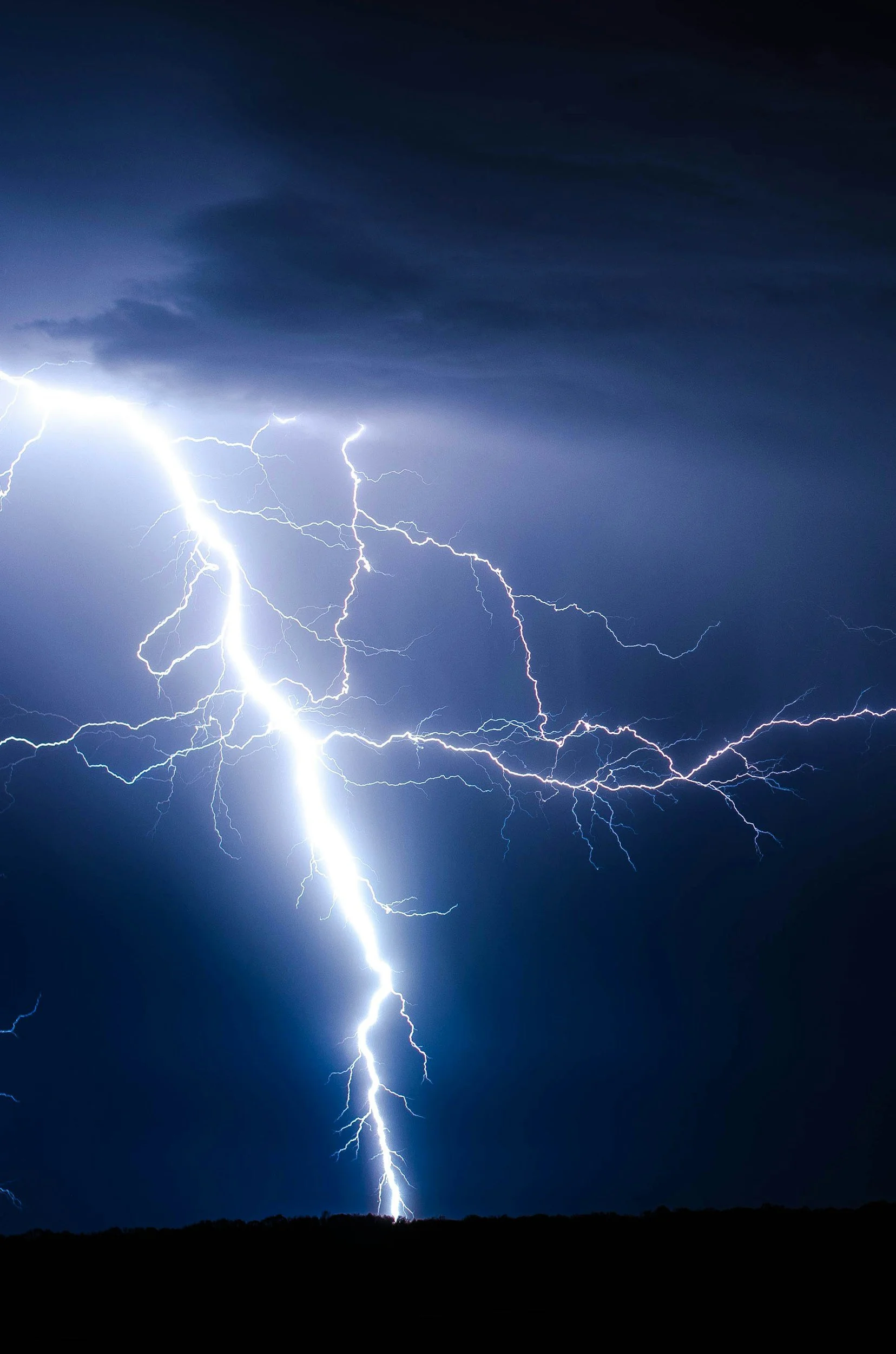 Lightning storm illuminating dark cloudy sky over a flat horizon.