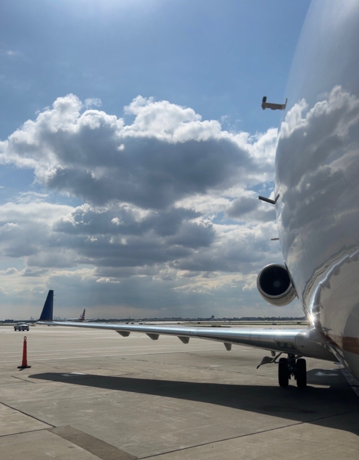 Image of an airplane on the tarmac at an airport, with clouds in the sky and other airplanes in the distance.