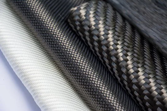 Close-up of three rolled sheets of carbon fiber fabric in black, gray, and white.