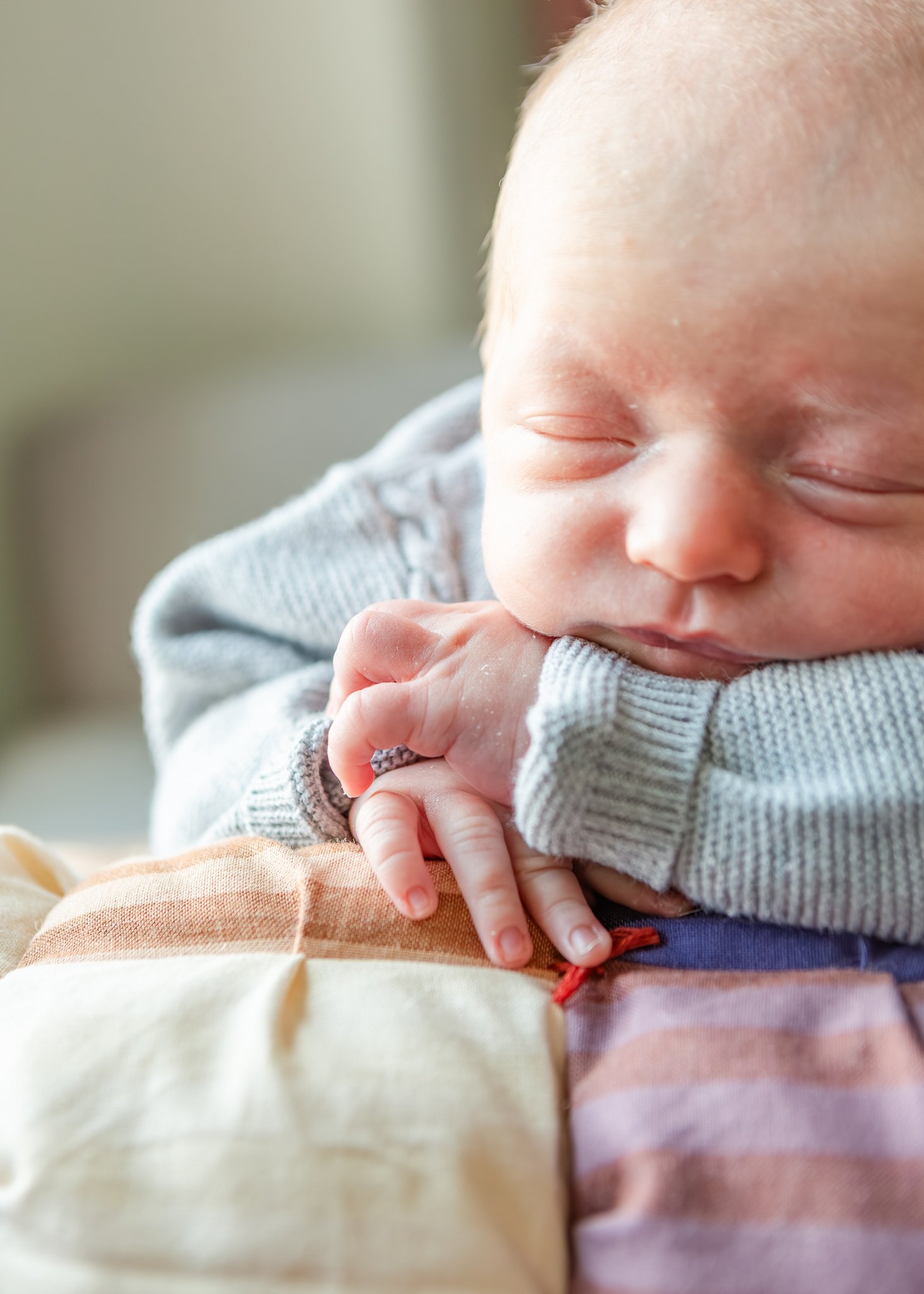 Close-up of a sleeping baby with eyes closed, wearing a gray striped shirt, with hands resting on chest, cozy and peaceful expression.