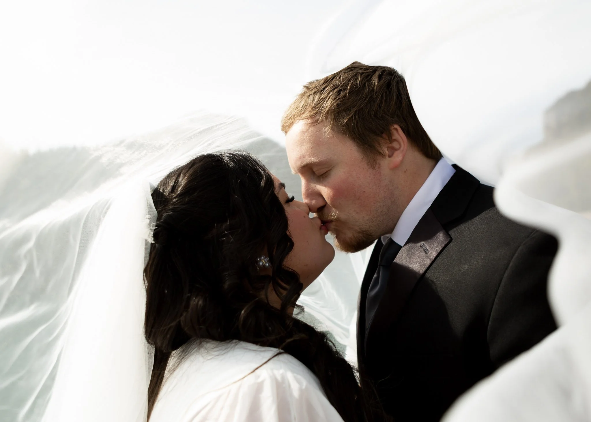 A bride and groom sharing a kiss, with the bride's veil partially covering their faces.