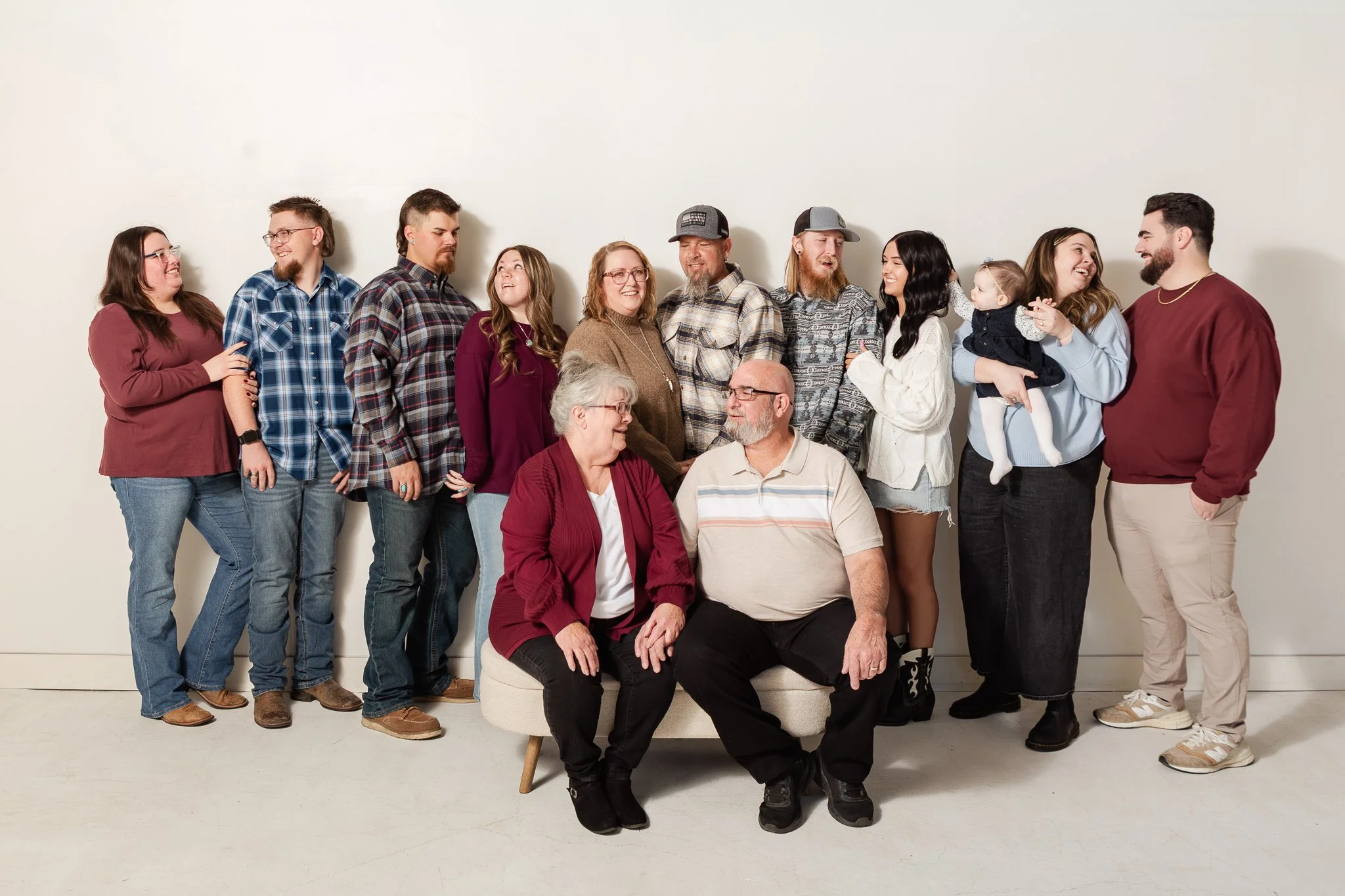 Affordable Utah Photographer, Utah County. A large multigenerational family gathered together, sitting and standing against a white background, smiling and interacting happily.