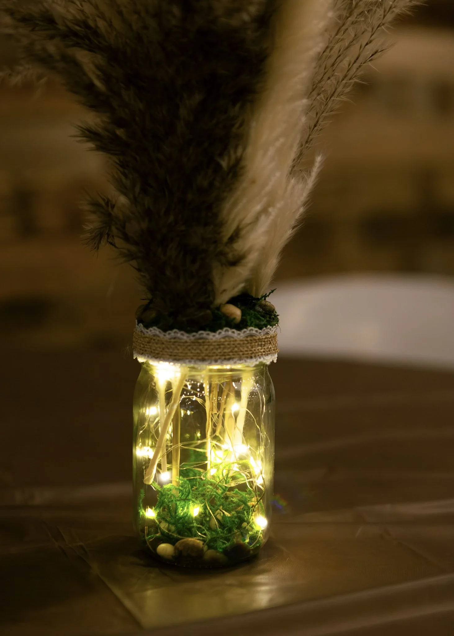 A jar filled with fairy lights, small rocks, and green plants at the bottom. A feathered bird sculpture with brown and black feathers is placed upside down on top of the jar, with its beak touching the jar's opening.
