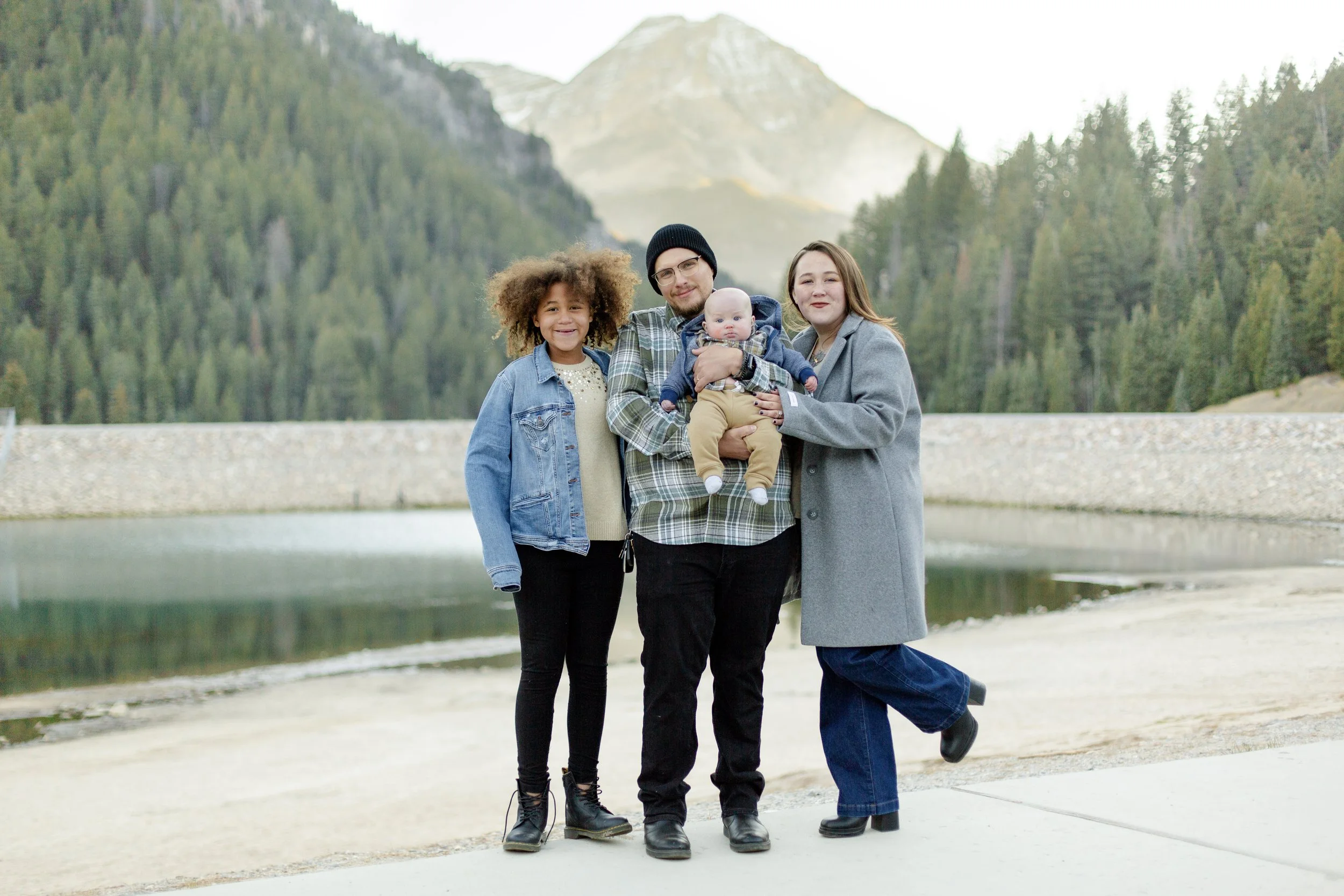 A smiling family of eight posing outdoors during sunset, with a scenic landscape in the background.