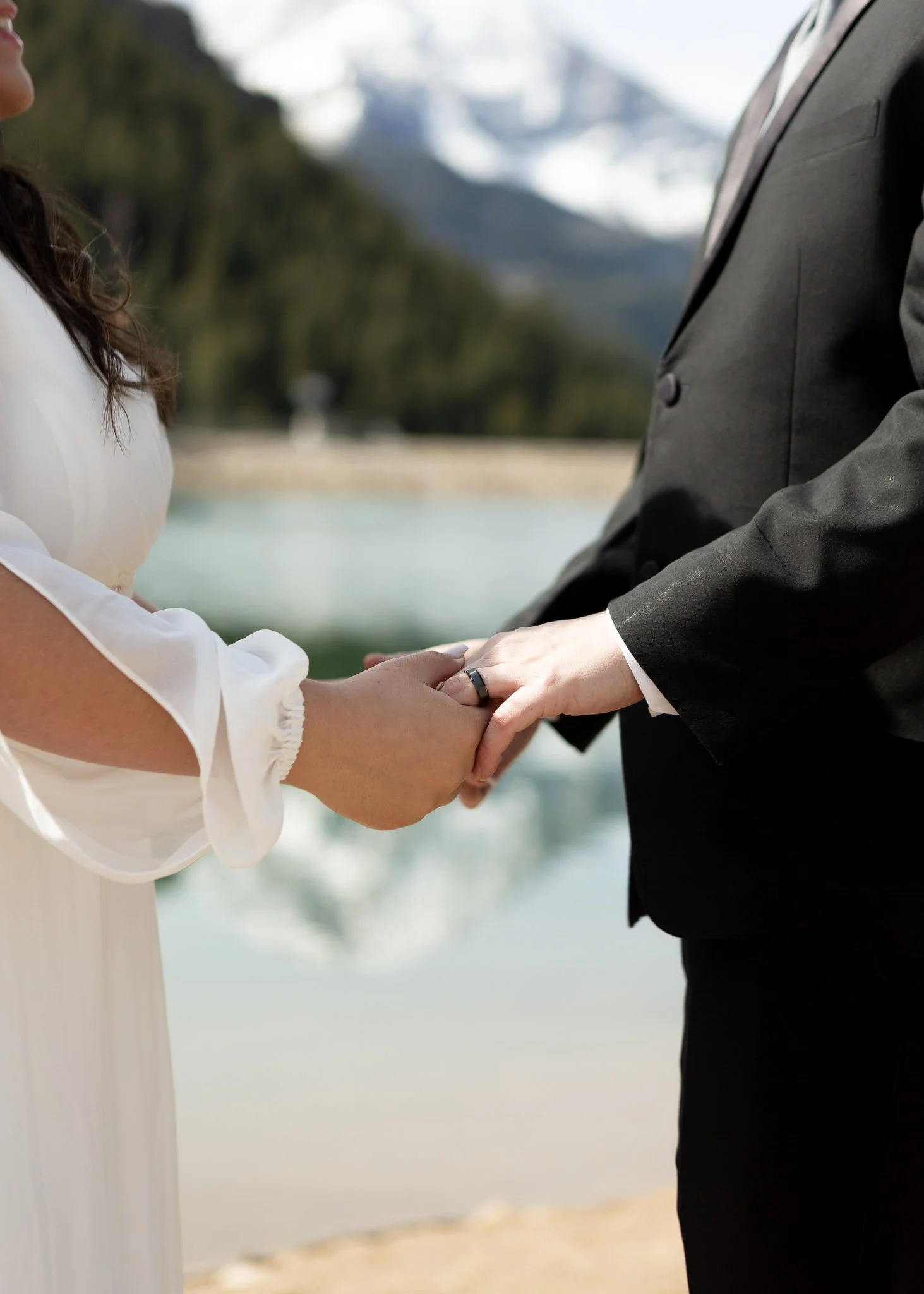 Bride and groom holding hands during a wedding ceremony outdoors with mountains and trees in the background.