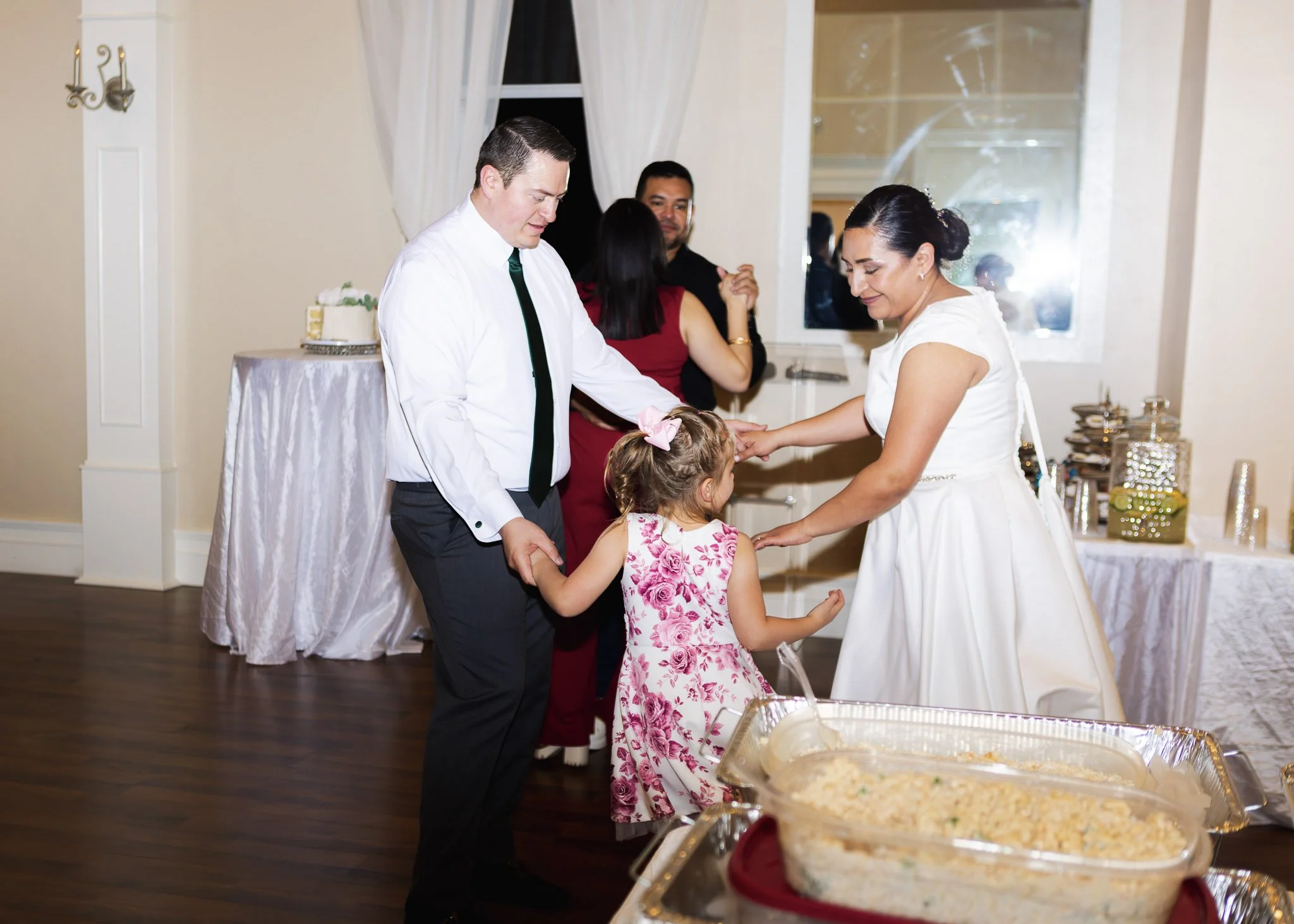 People at a celebration, possibly a wedding reception, exchanging rings or vows, with food in serving trays in the foreground.