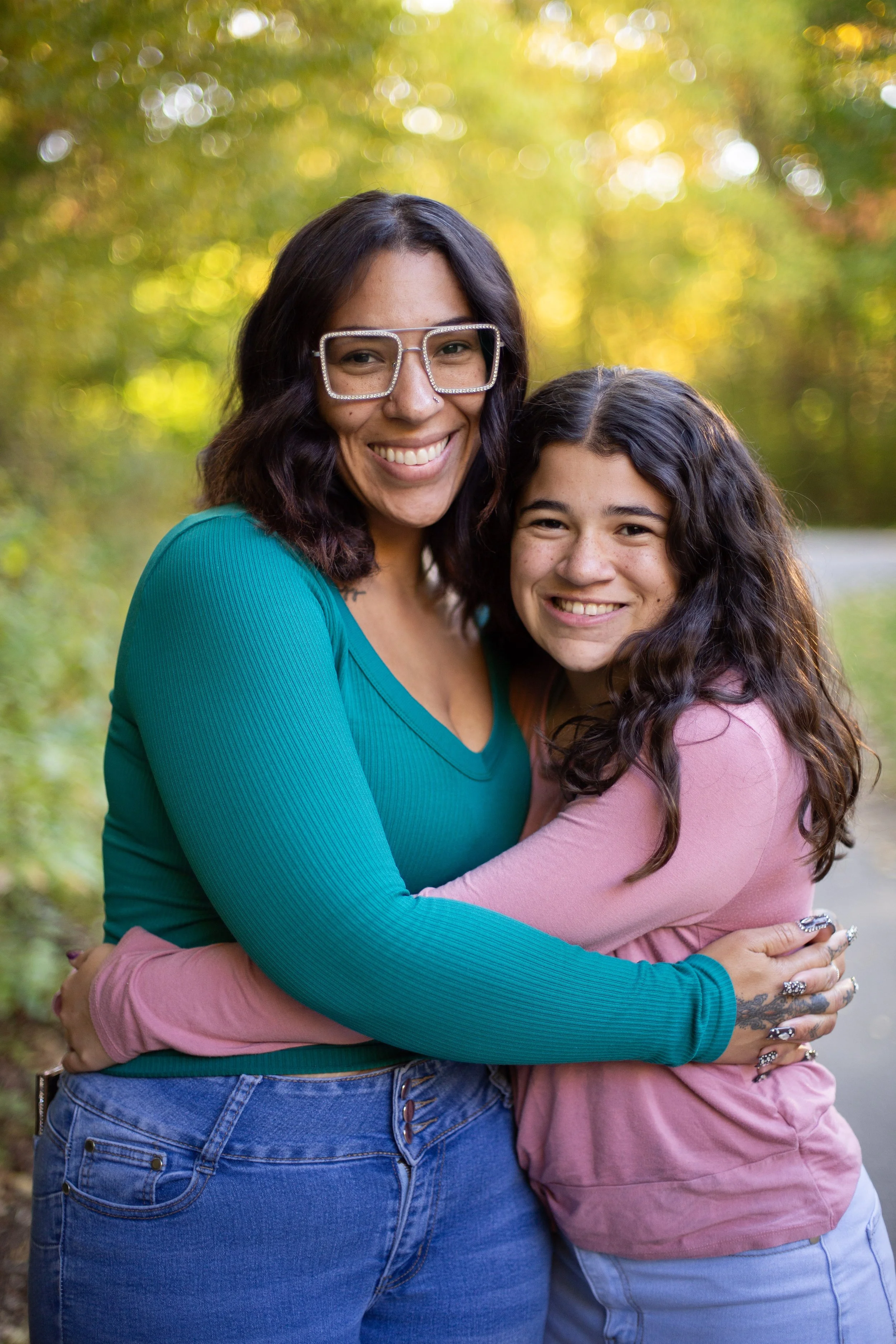 Two women hugging outdoors with trees in the background, smiling at the camera.