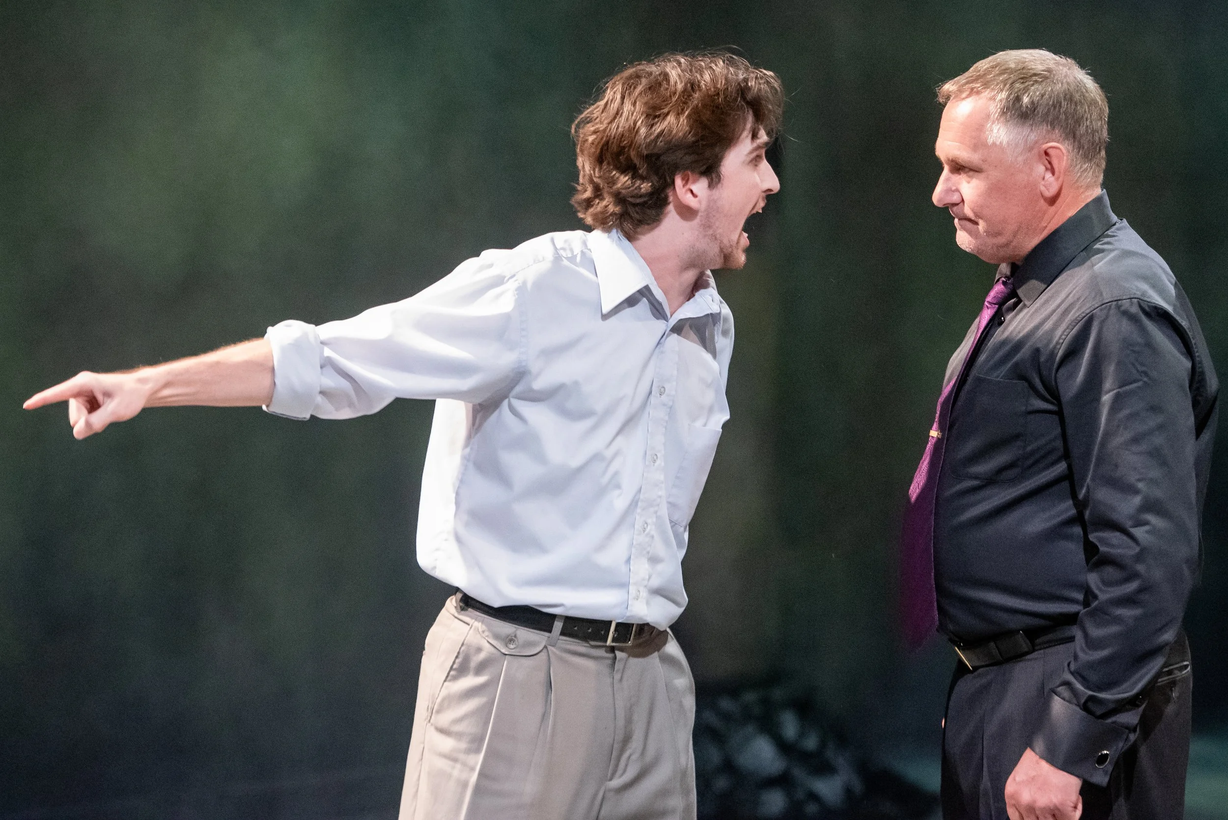 Two men are engaged in an intense argument, with the man on the left pointing and yelling at the man on the right, who appears unfazed.