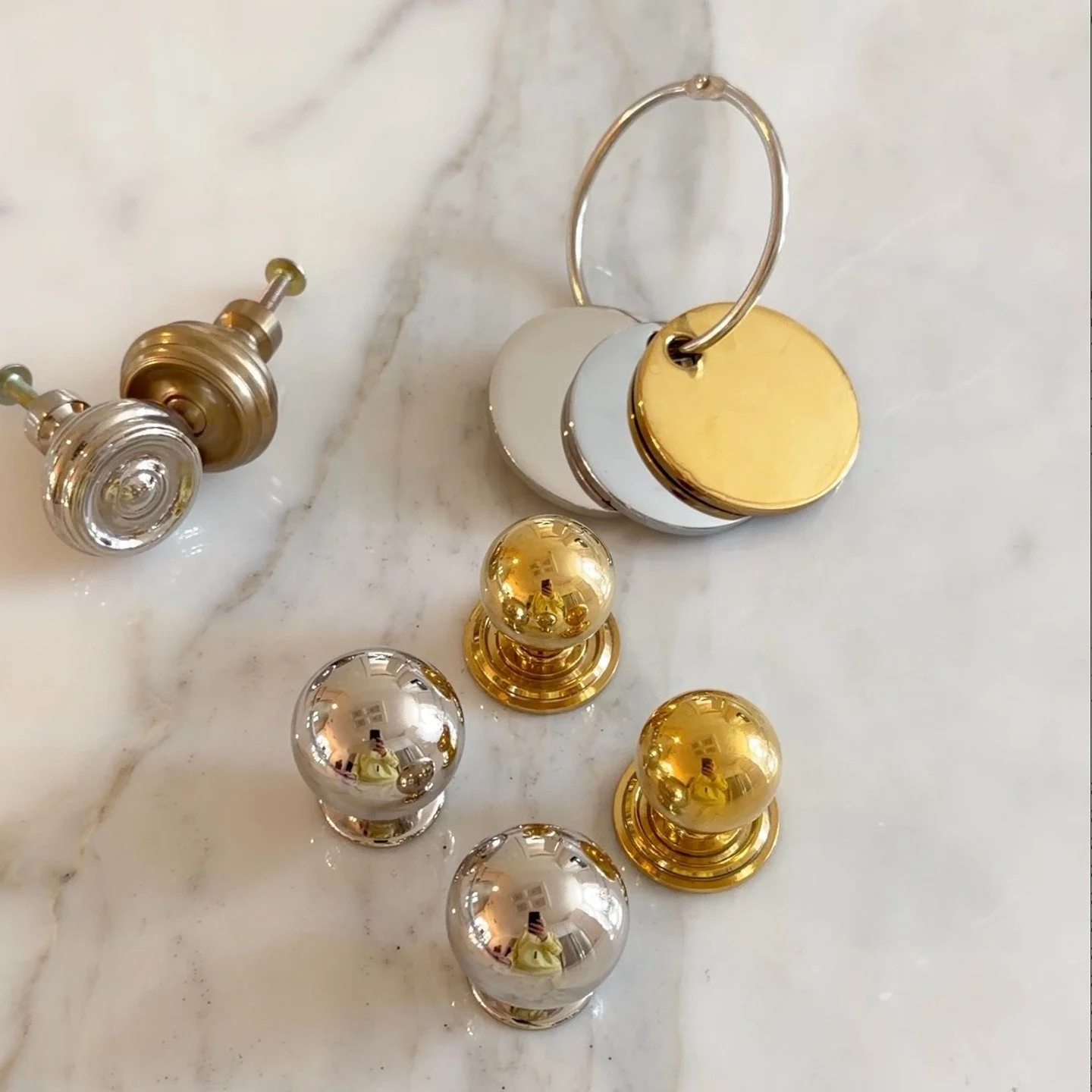 Decorative cabinet knobs and hooks in gold and silver finishes on a marble surface.