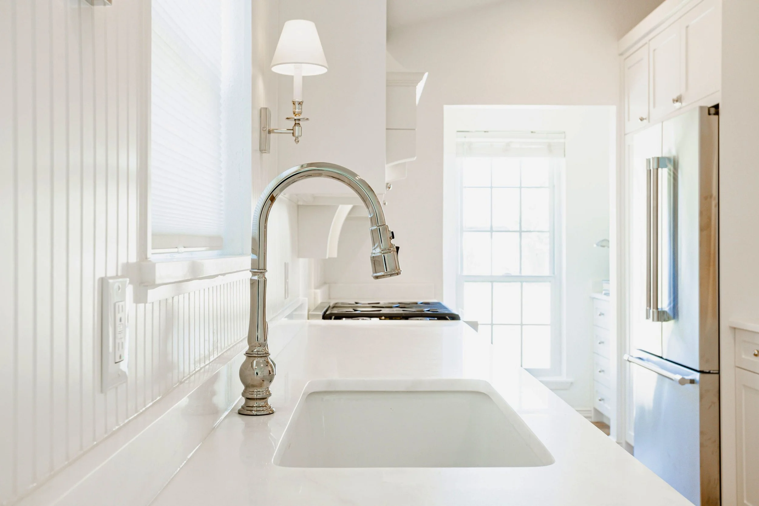 White kitchen sink and faucet detail with classic cabinetry, countertop, and natural light.