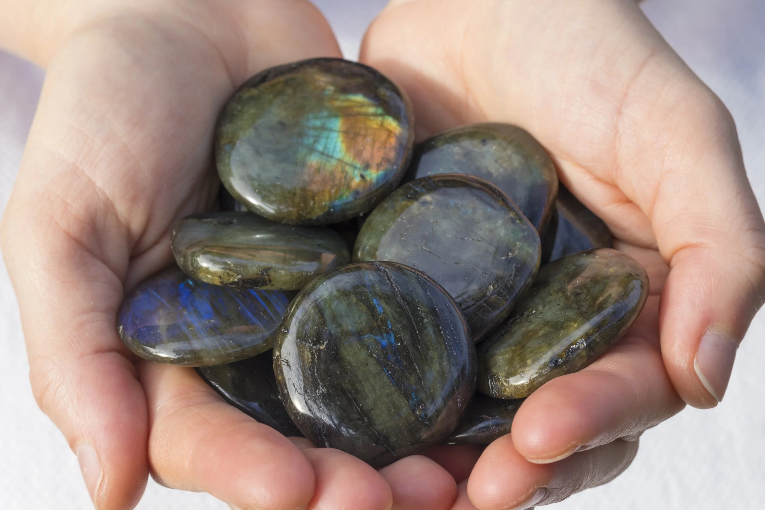 Hand holding polished labradorite stones with iridescent blue, green, and gold hues representing personal reflection and individuality in sacred perspectives.