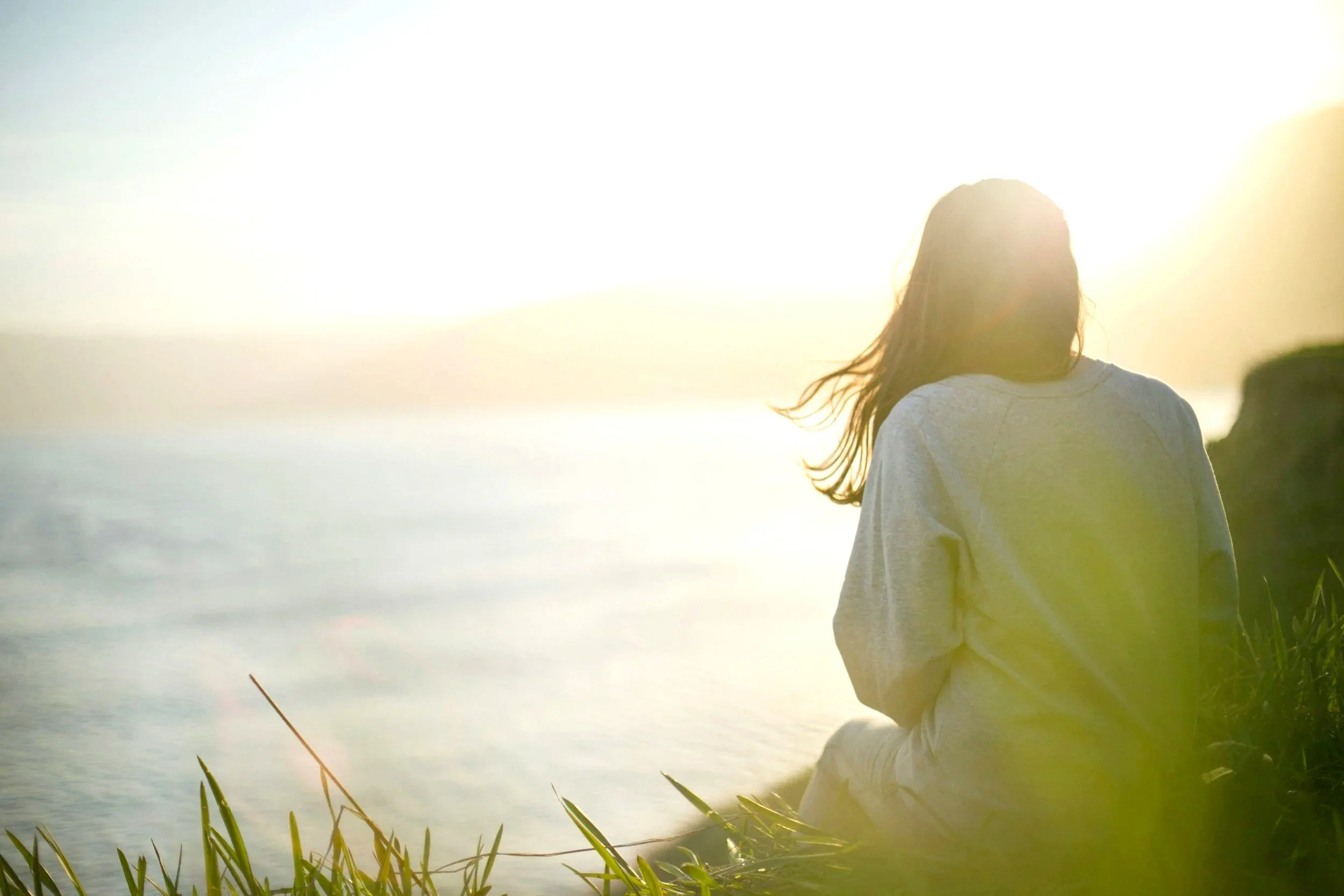 Woman sitting quietly near the ocean at sunset in reflection and spiritual contemplation