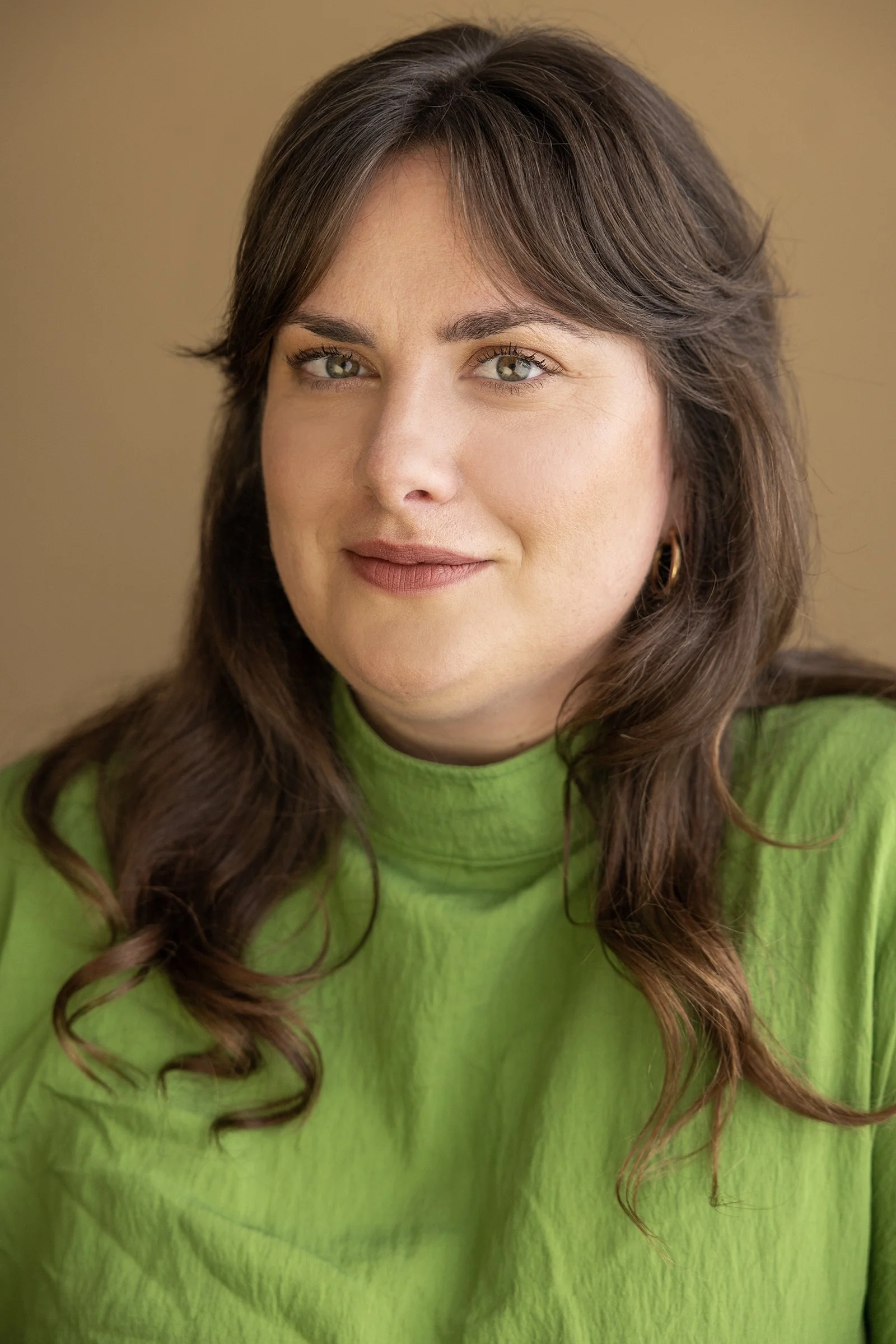 Hannah has long brown hair and green eyes. She is wearing a green dress, and is smiling.