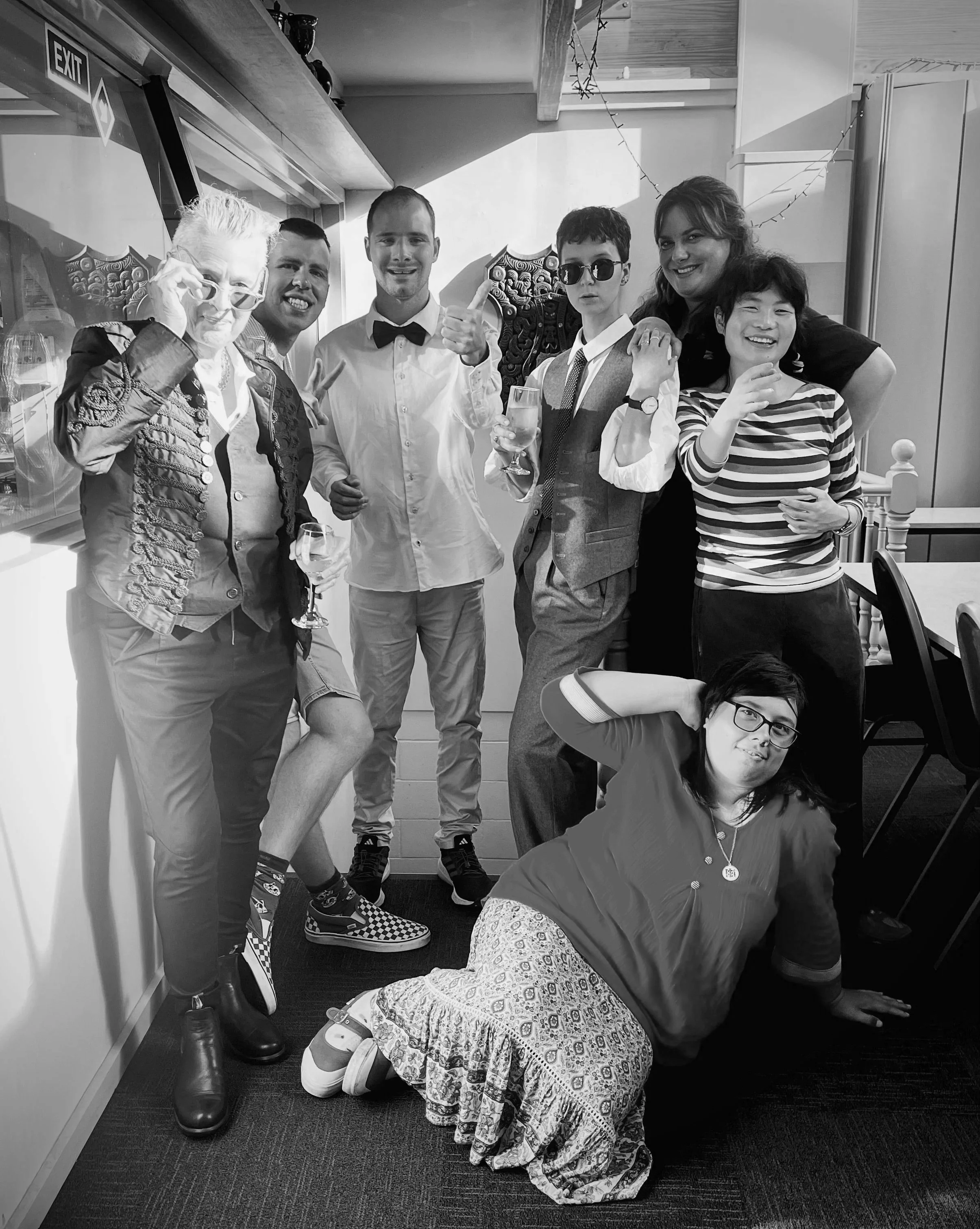 A group of four actors and three directors stand together, dressed in fancy clothes. The photo is black and white.
