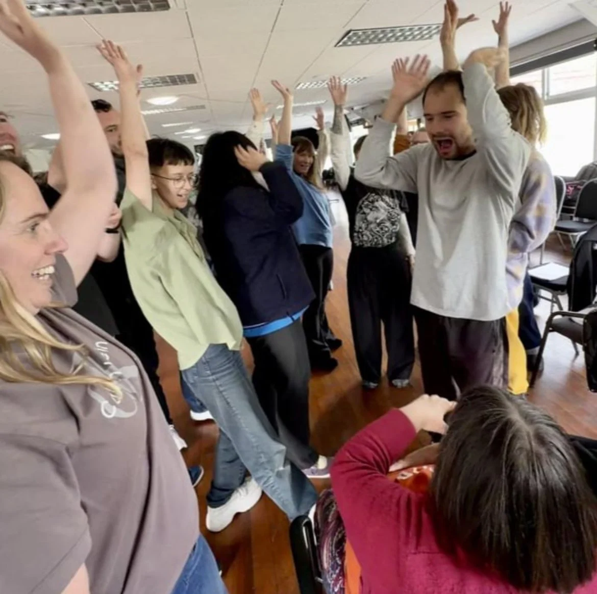 A group photo where all the company members have their hands in the air and are calling out "Drama-de-wama!!"