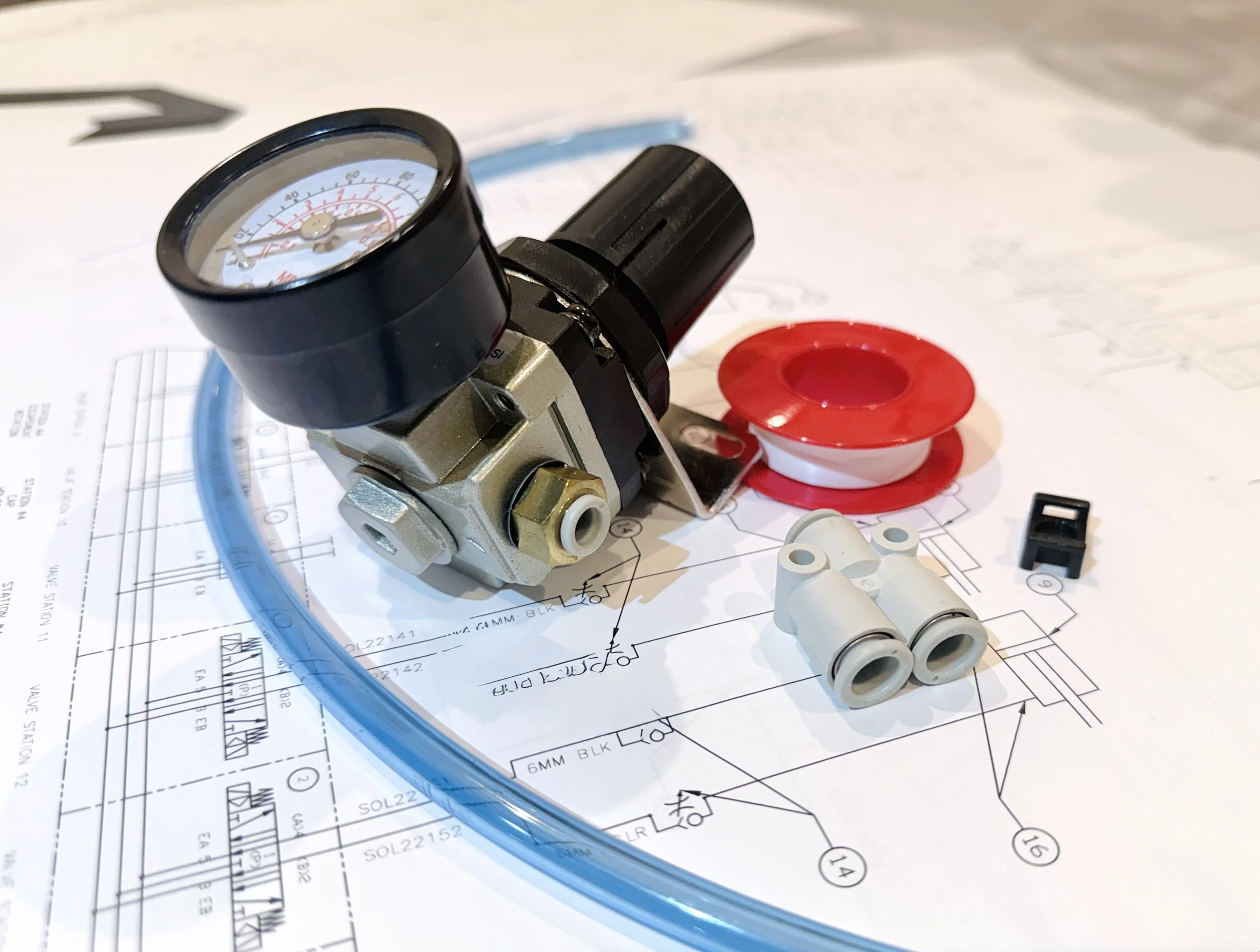 A pneumatic regulator, Teflon tape spool, quick connect fittings, black switch, and clear blue tubing placed on an pneumatic schematic drawing.