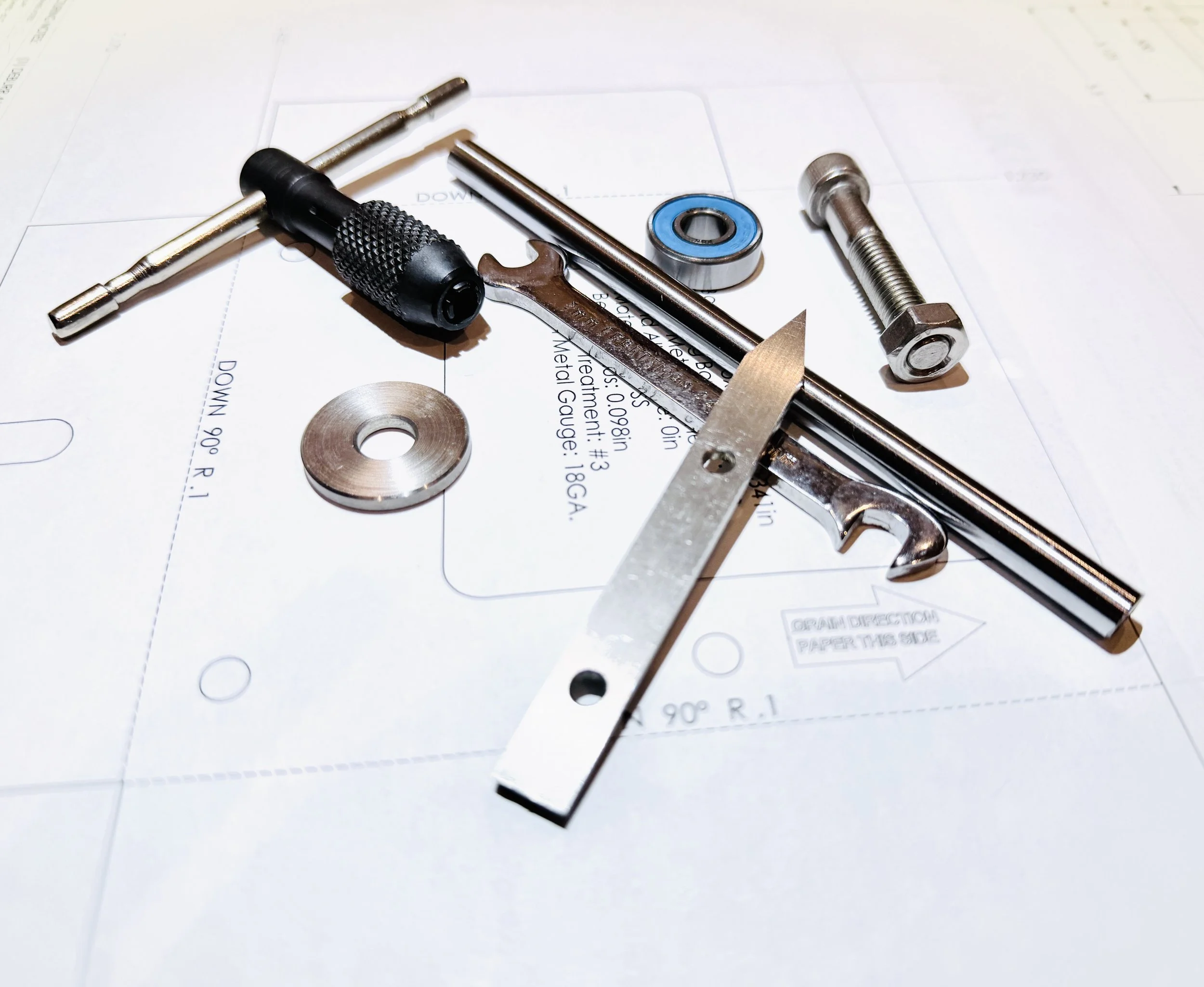 Tapping handle, stainless steel spacers, a thread gauge, a bolt, a bearing, and a small wrench arranged on a technical drawing.