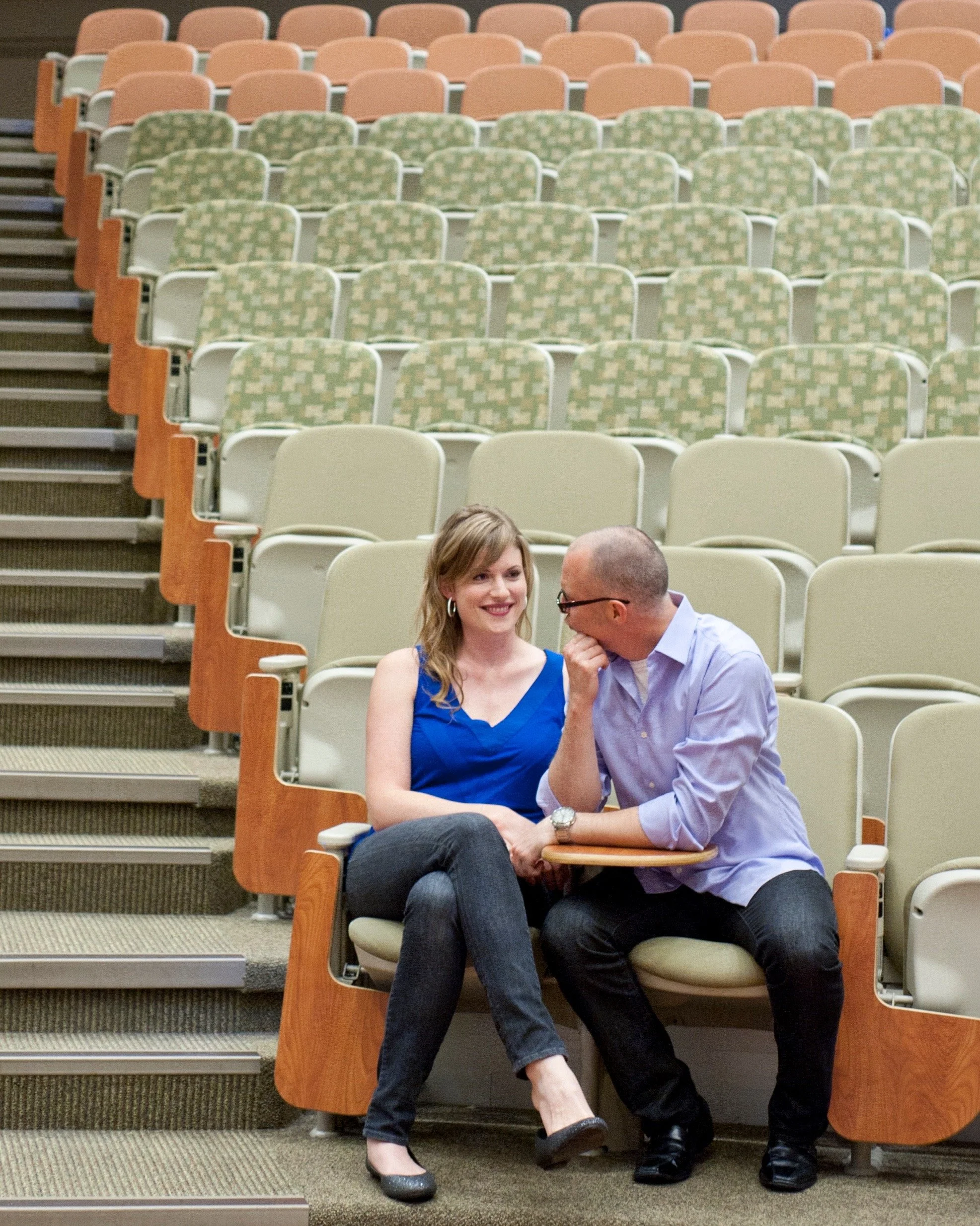 A woman and man sitting on chairs in a lecture theatre.