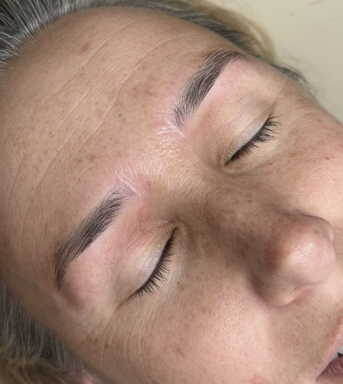 Close-up of a woman's face with closed eyes, showing well-groomed eyebrows and smooth skin.