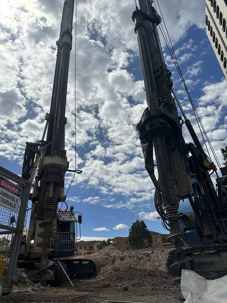 Construction site with two large drilling machines against a partly cloudy sky.