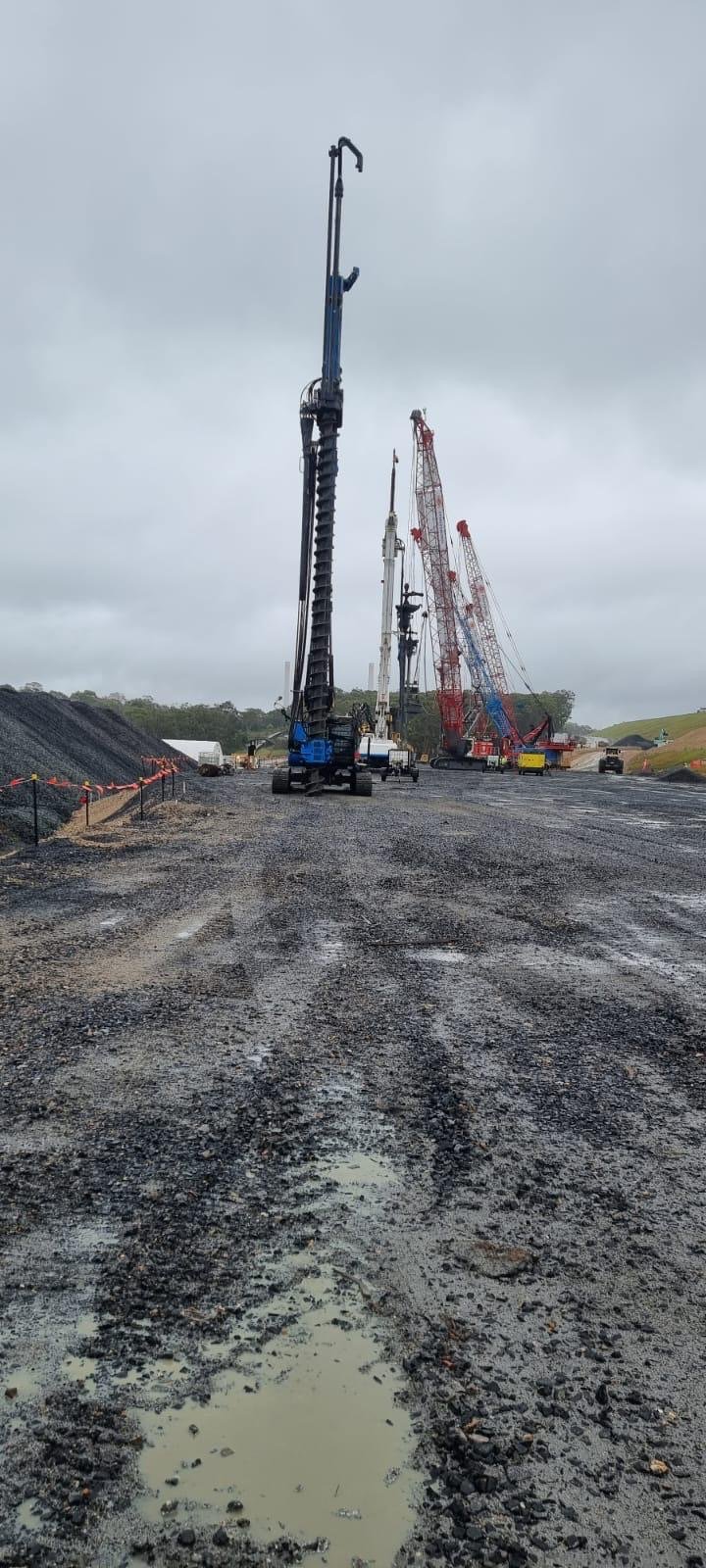 Construction site with large cranes on a muddy road under cloudy sky.