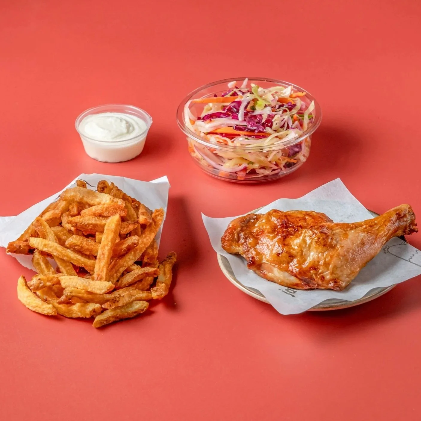 Fried chicken wing, French fries with a side of ranch dressing, a small bowl of coleslaw salad, and a cup of ranch dipping sauce on a pink background.
