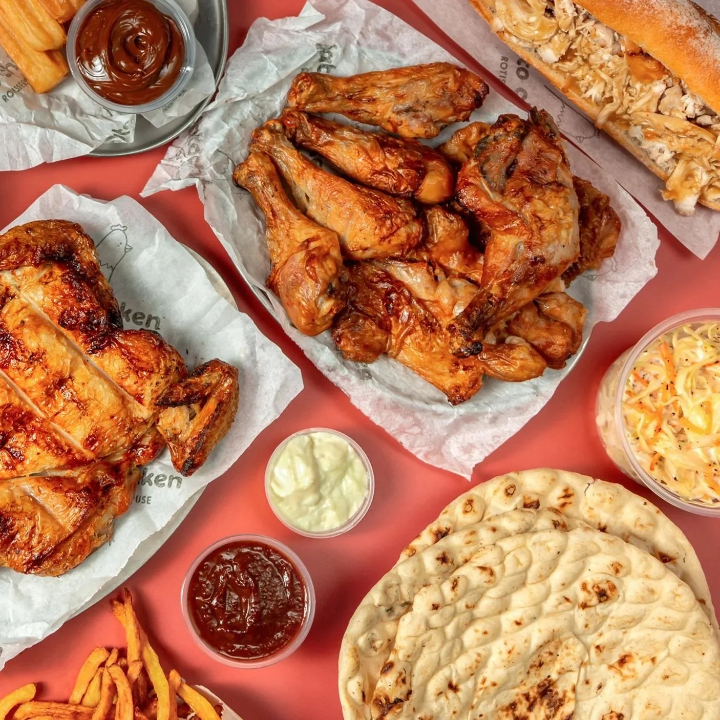 Plate of grilled chicken wings, flatbread, coleslaw, French fries, and dipping sauces on a pink table.
