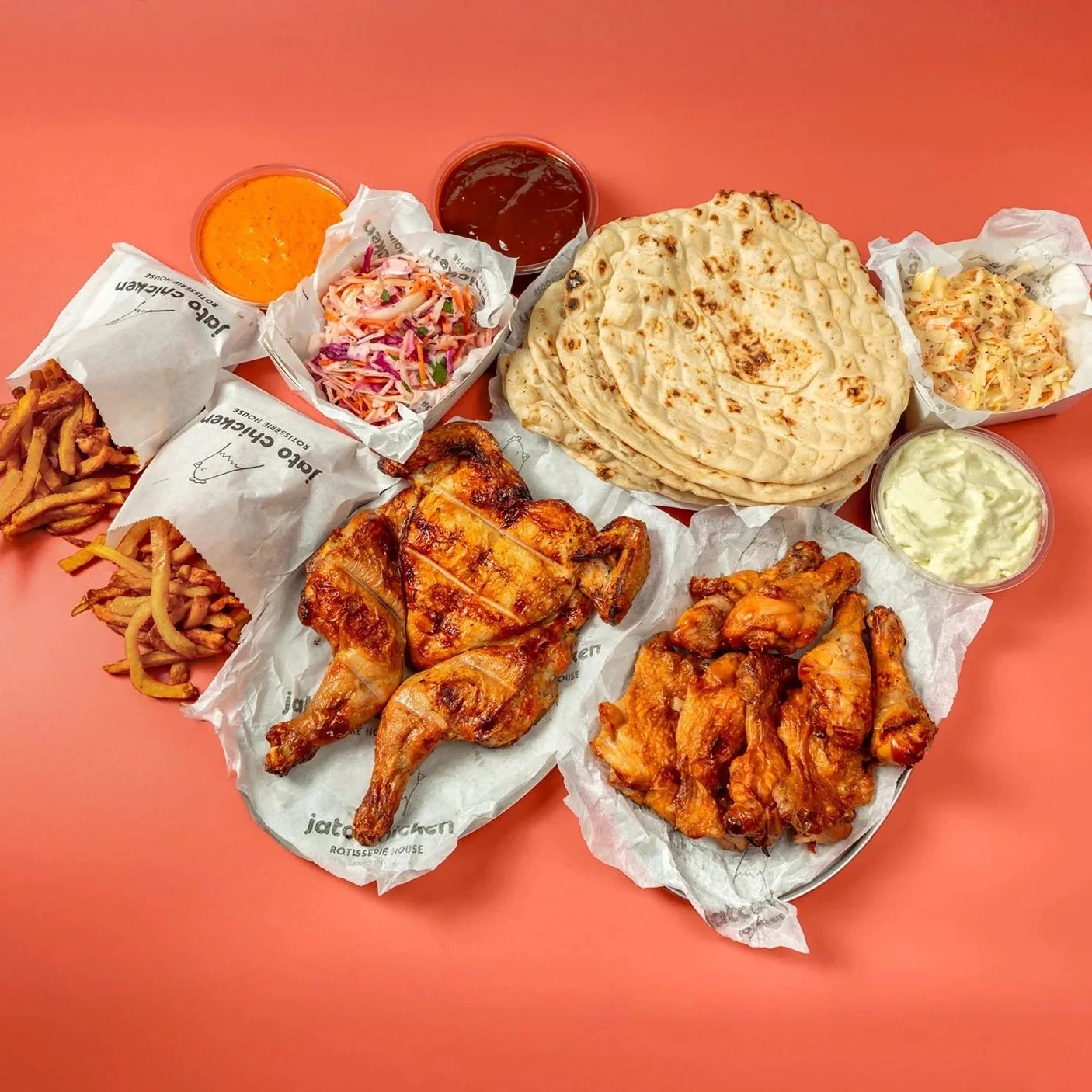 Plate of Indian food with naan bread, two types of curry, fried chicken, coleslaw, and side sauces on a pink table.