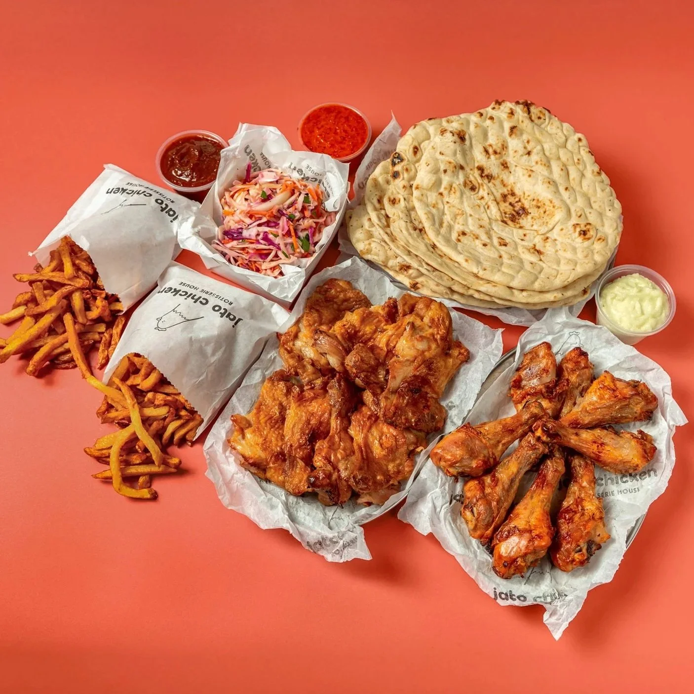 Assorted Indian cuisine including naan bread, chicken wings, fried chicken, coleslaw, fries with gravy, and three small cups of sauces, on a pink background.