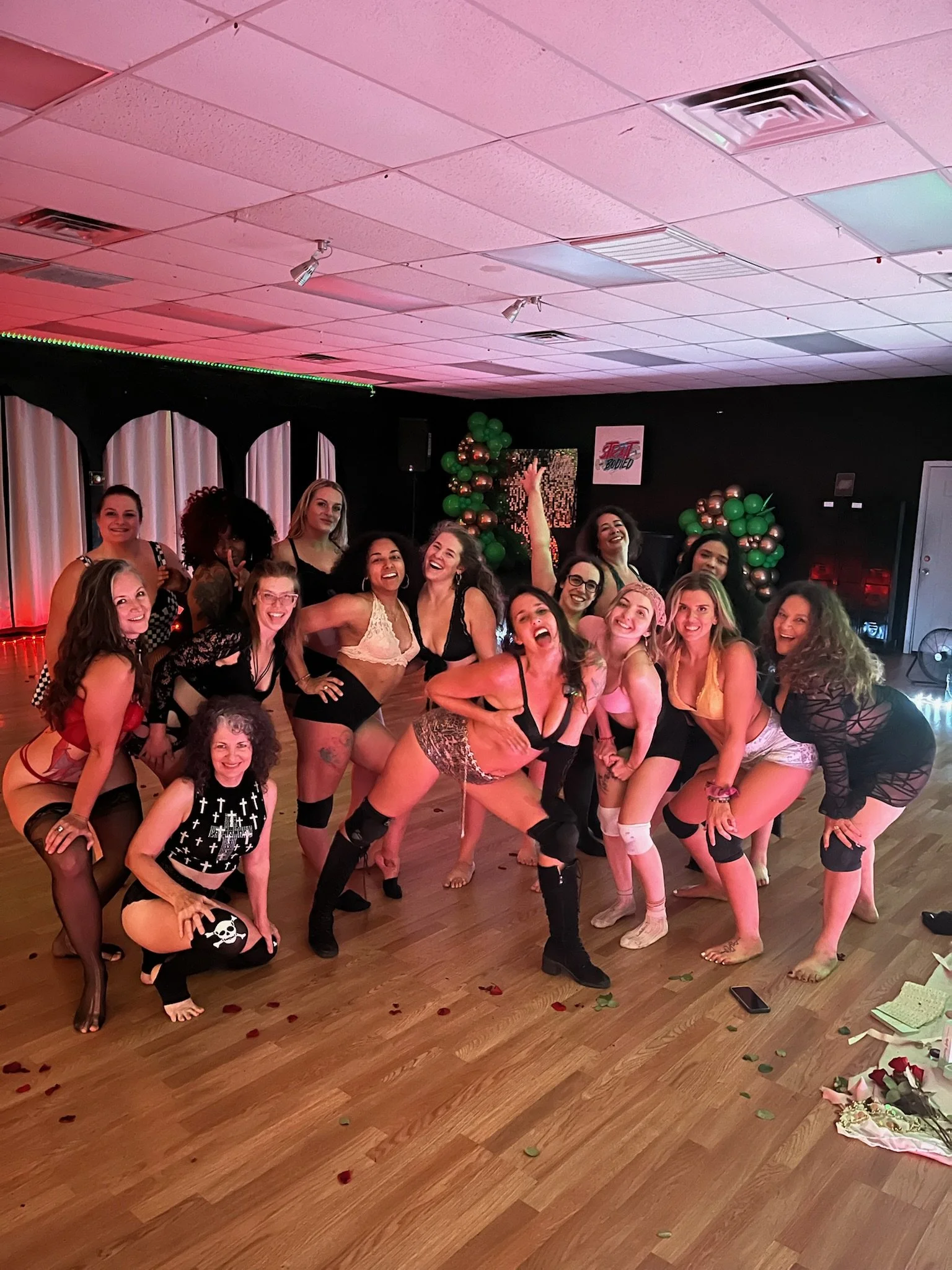 A group of women wearing lingerie and knee-high socks, posing and dancing enthusiastically in a decorated indoor space, likely celebrating an event.